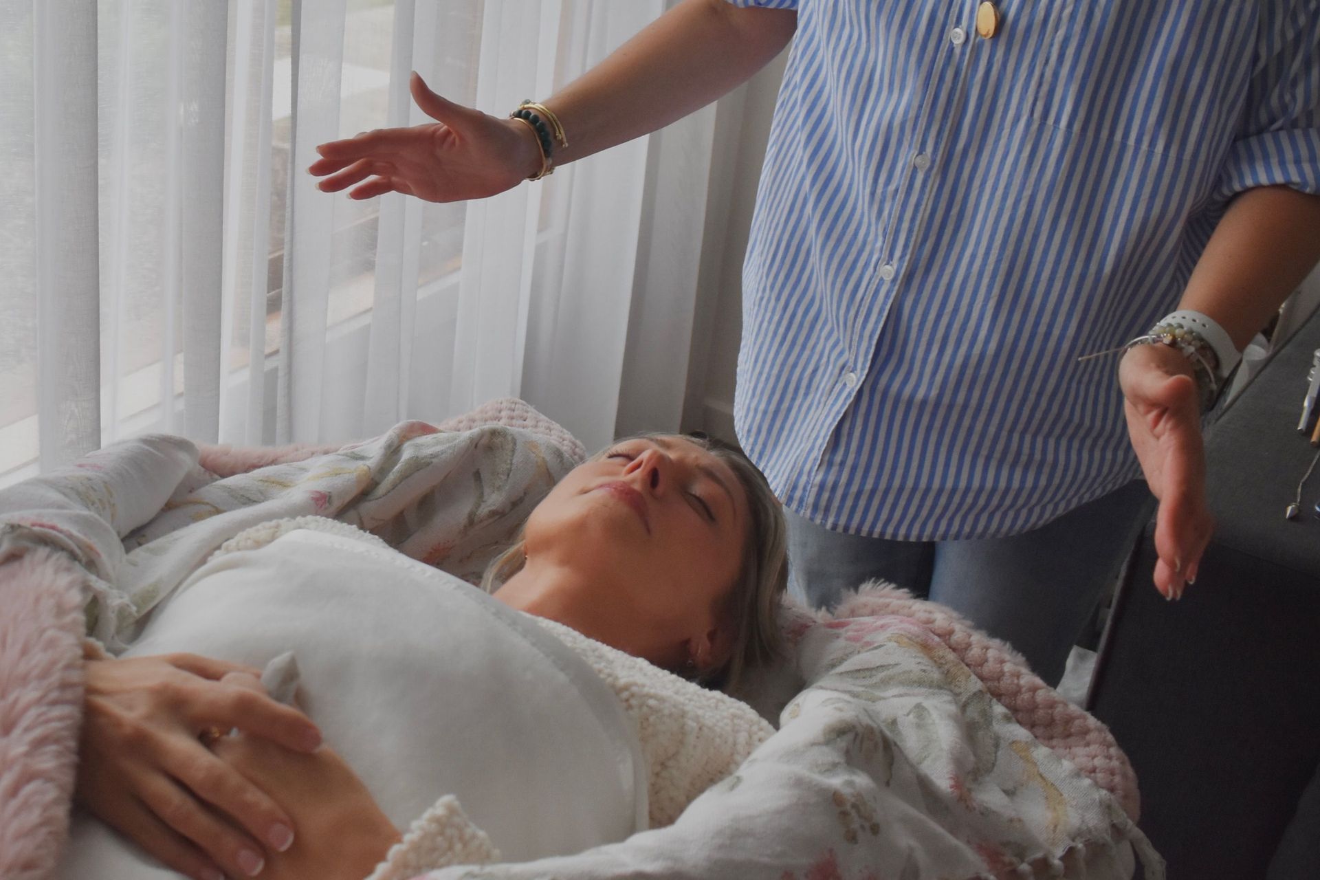 Person lying in bed while two people stand beside them with arms raised in a bright room