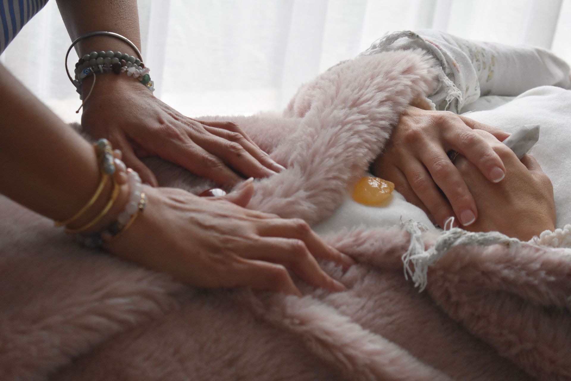 Hands touching a person lying under a pink blanket, with a yellow stone on the chest.