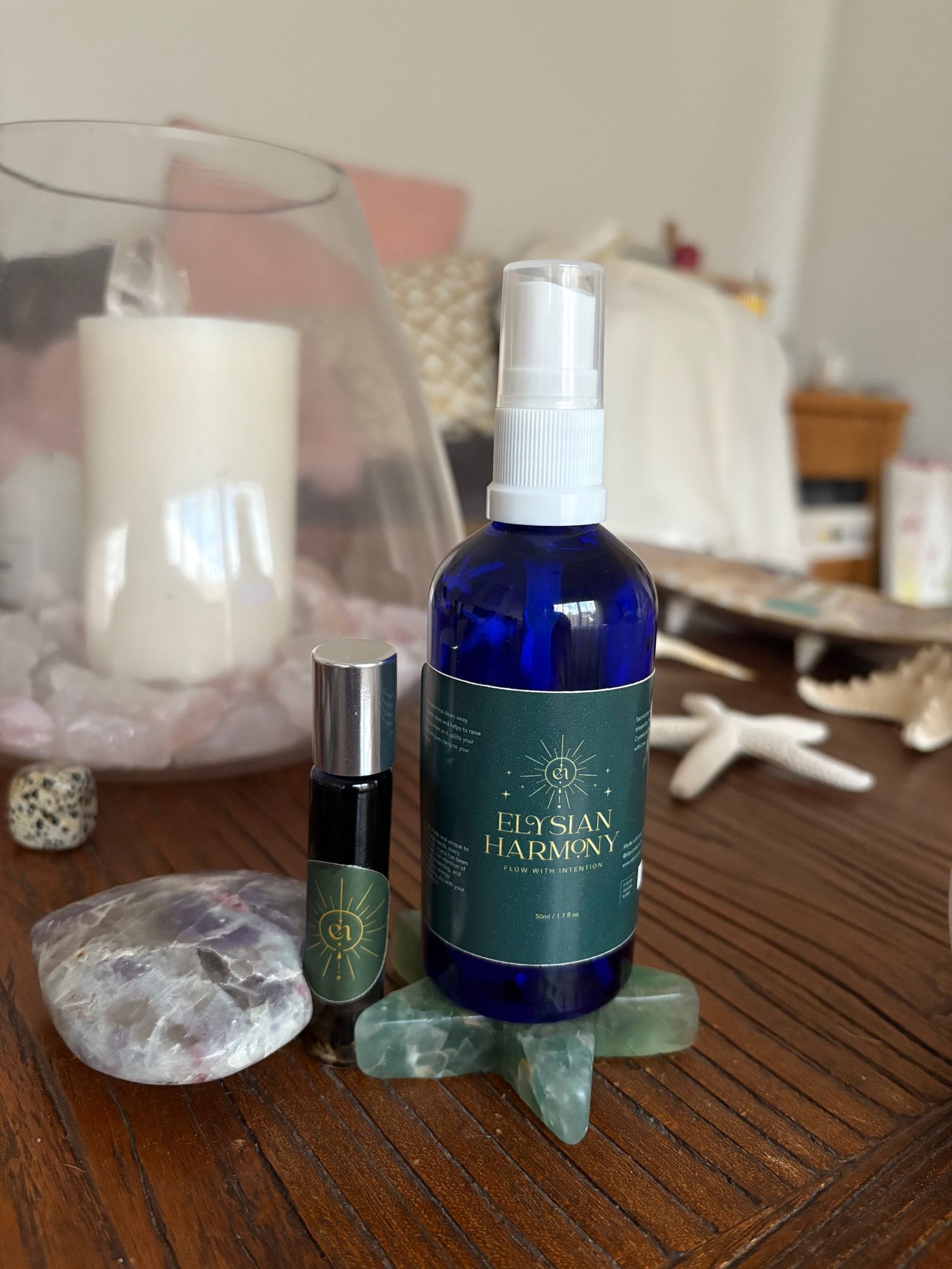 Blue spray bottle and small green perfume bottle on a wooden table with a candle and crystal decor