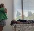 Person in a green shirt stands by a window near a couch with a sleeping dog.