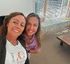 Two women smiling for a selfie by a window with city buildings in the background