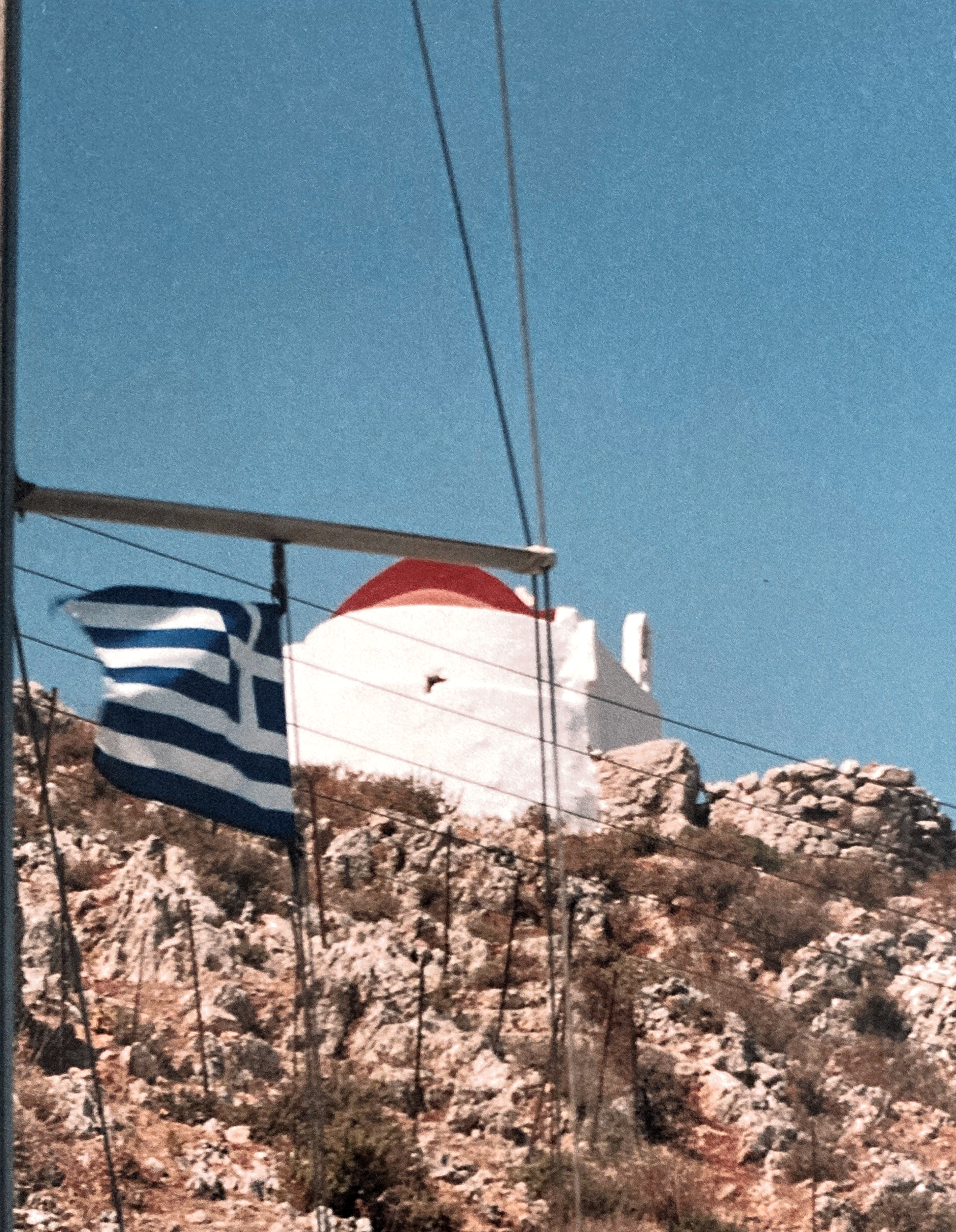 Eine griechische Flagge weht vor einem weißen Gebäude auf einem Hügel
