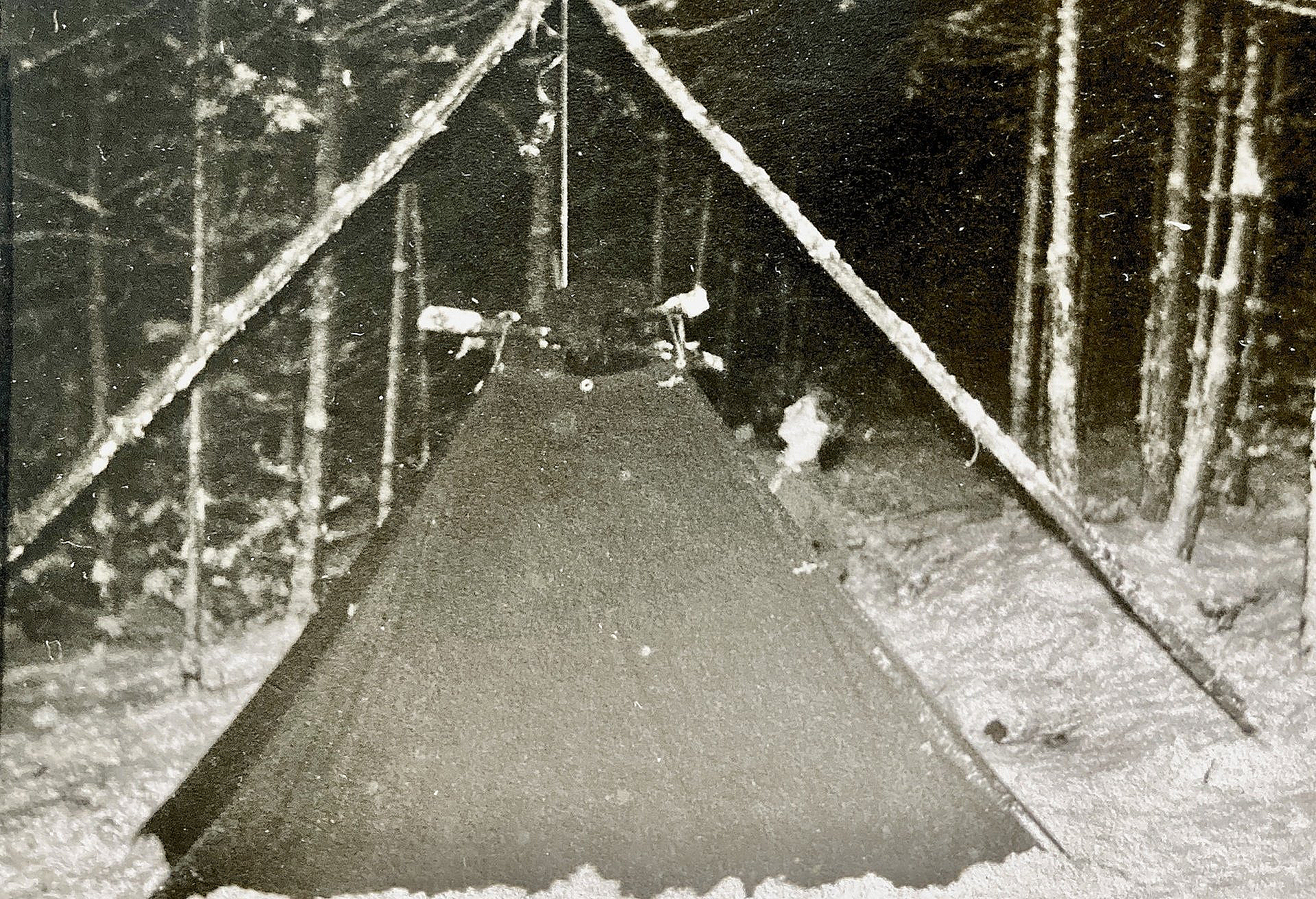 Ein Schwarzweißfoto eines Zeltes im Schnee im Wald.