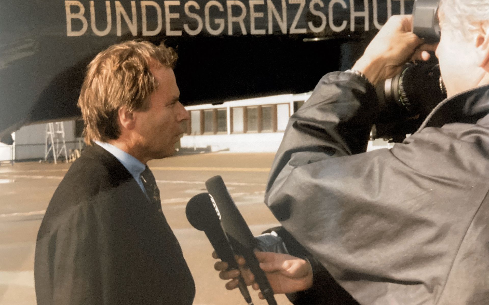 Ein Mann wird vor einem Schild mit der Aufschrift „Bundesgrenzschutz“ interviewt