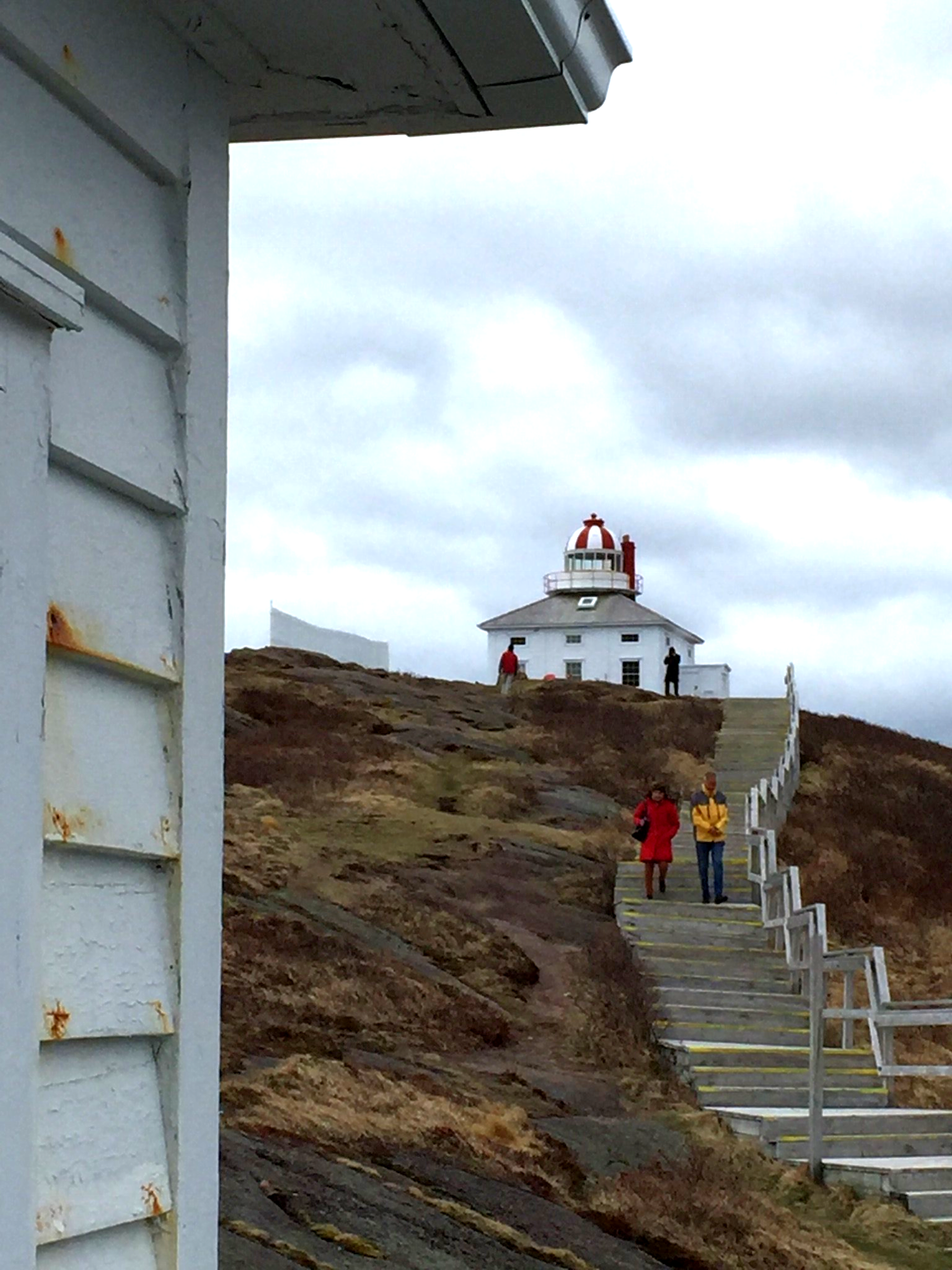Menschen gehen die Treppe zu einem Leuchtturm auf einem Hügel hinauf