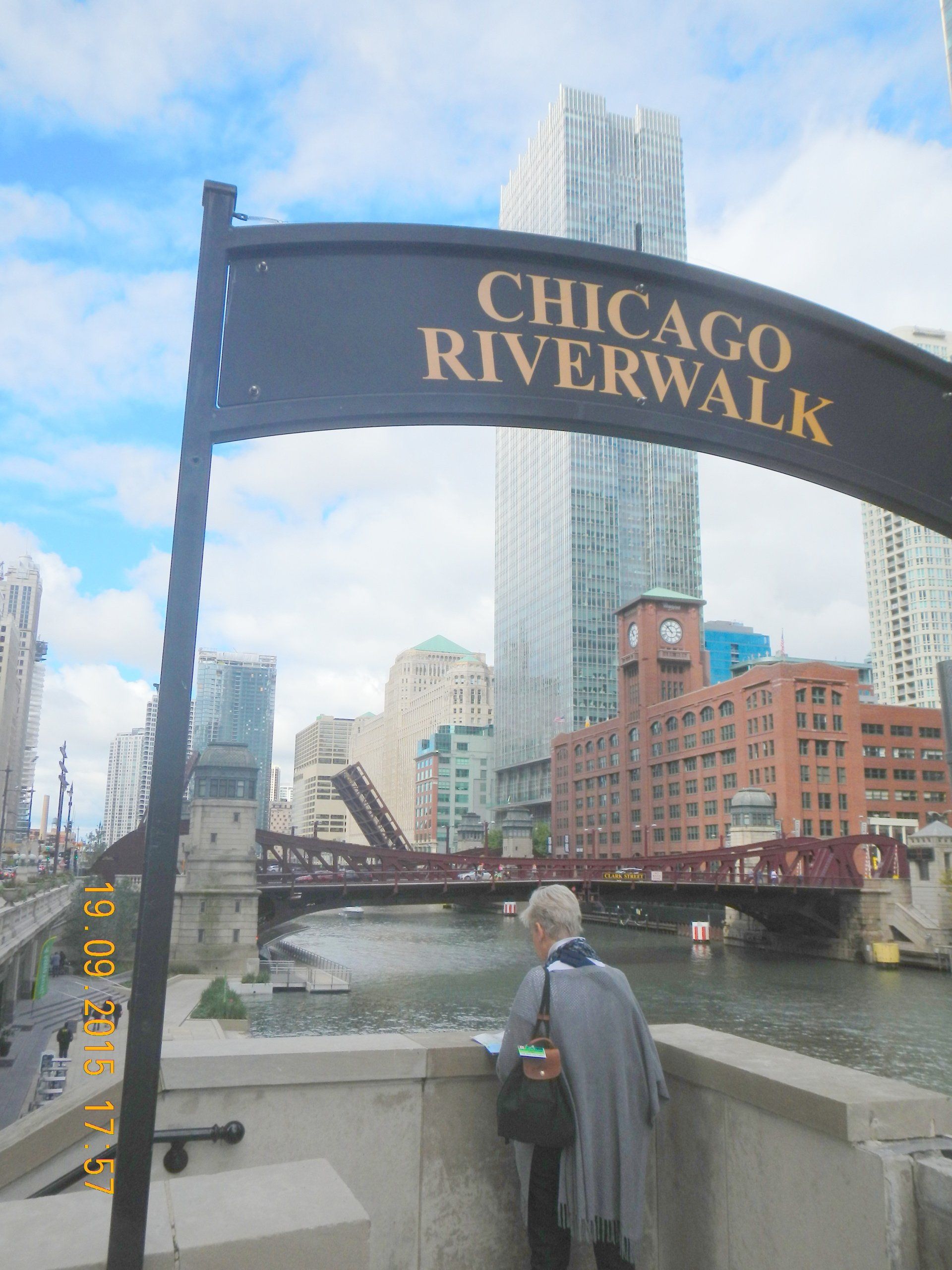 Eine Frau steht unter einem Schild mit der Aufschrift „Chicago Riverwalk“