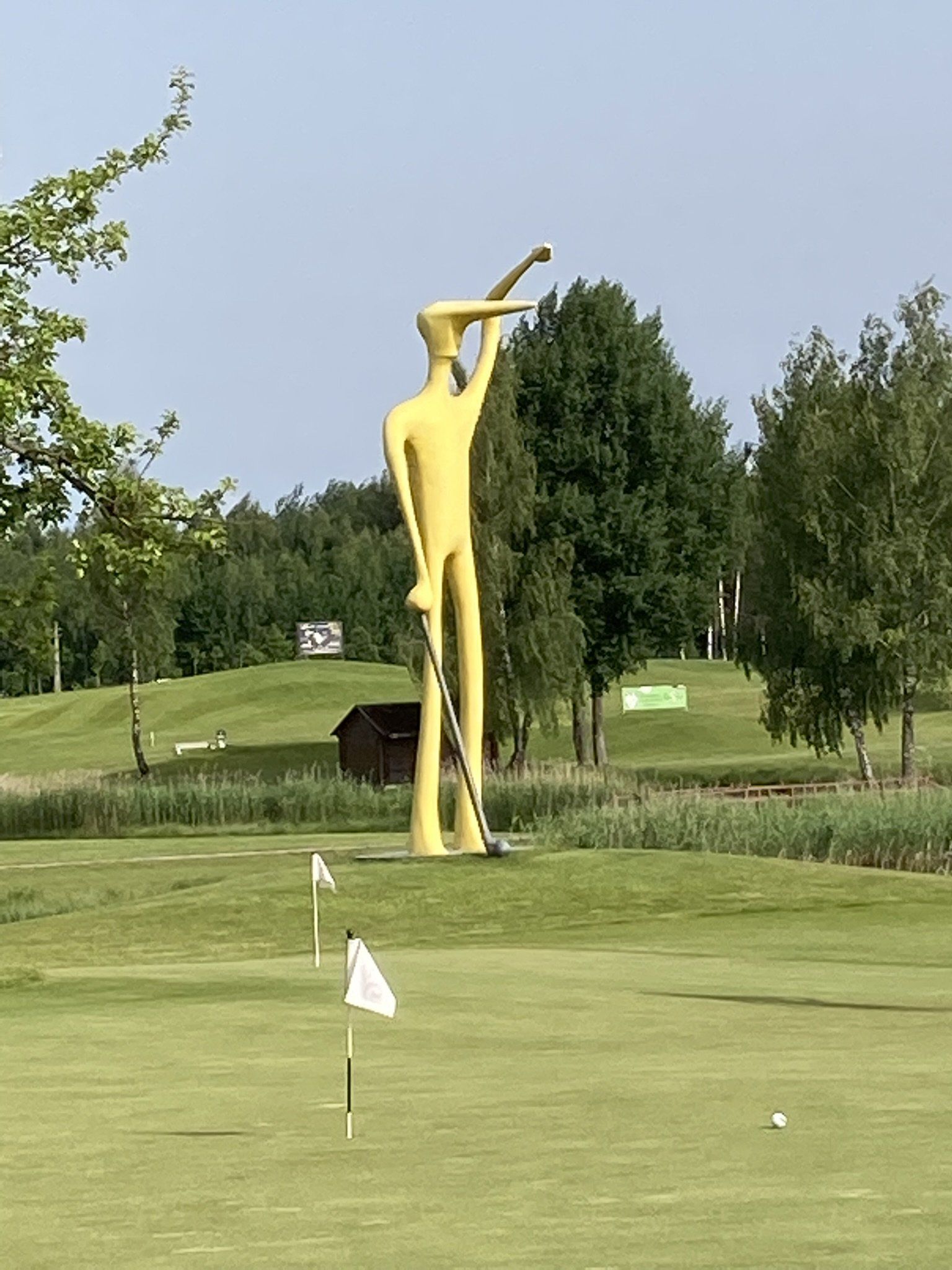 Eine große gelbe Statue eines Mannes, der auf einem Golfplatz einen Golfschläger hält.
