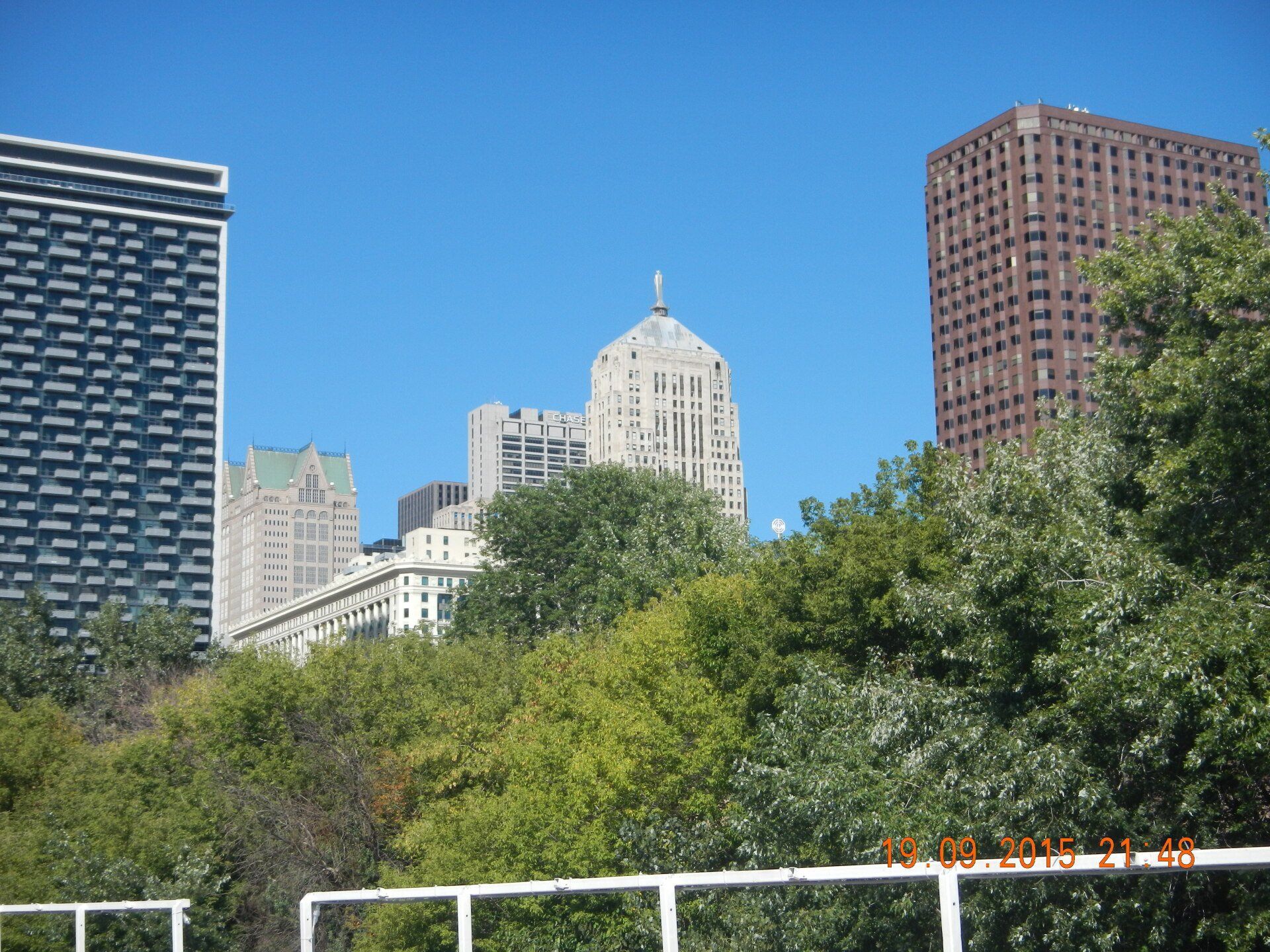 Eine Skyline einer Stadt mit einem Zaun und Bäumen im Vordergrund