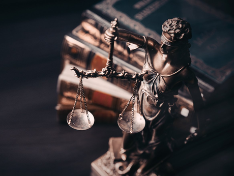 Eine Statue der Gerechtigkeit, die vor einem Stapel Bücher eine Waage hält.