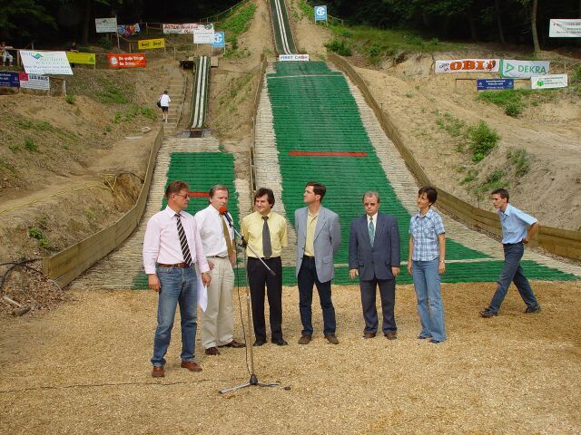 Eine Gruppe von Männern steht vor einem Mikrofon vor einer Skipiste