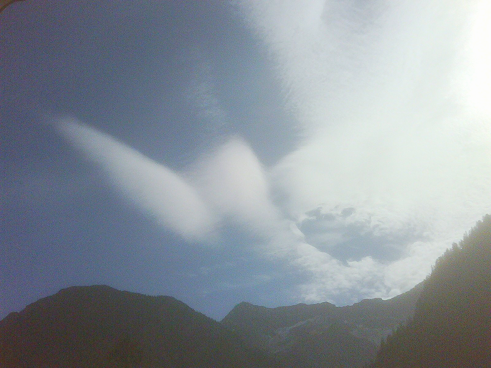 Eine Wolke in Form eines Engels schwebt am Himmel über einer Bergkette.