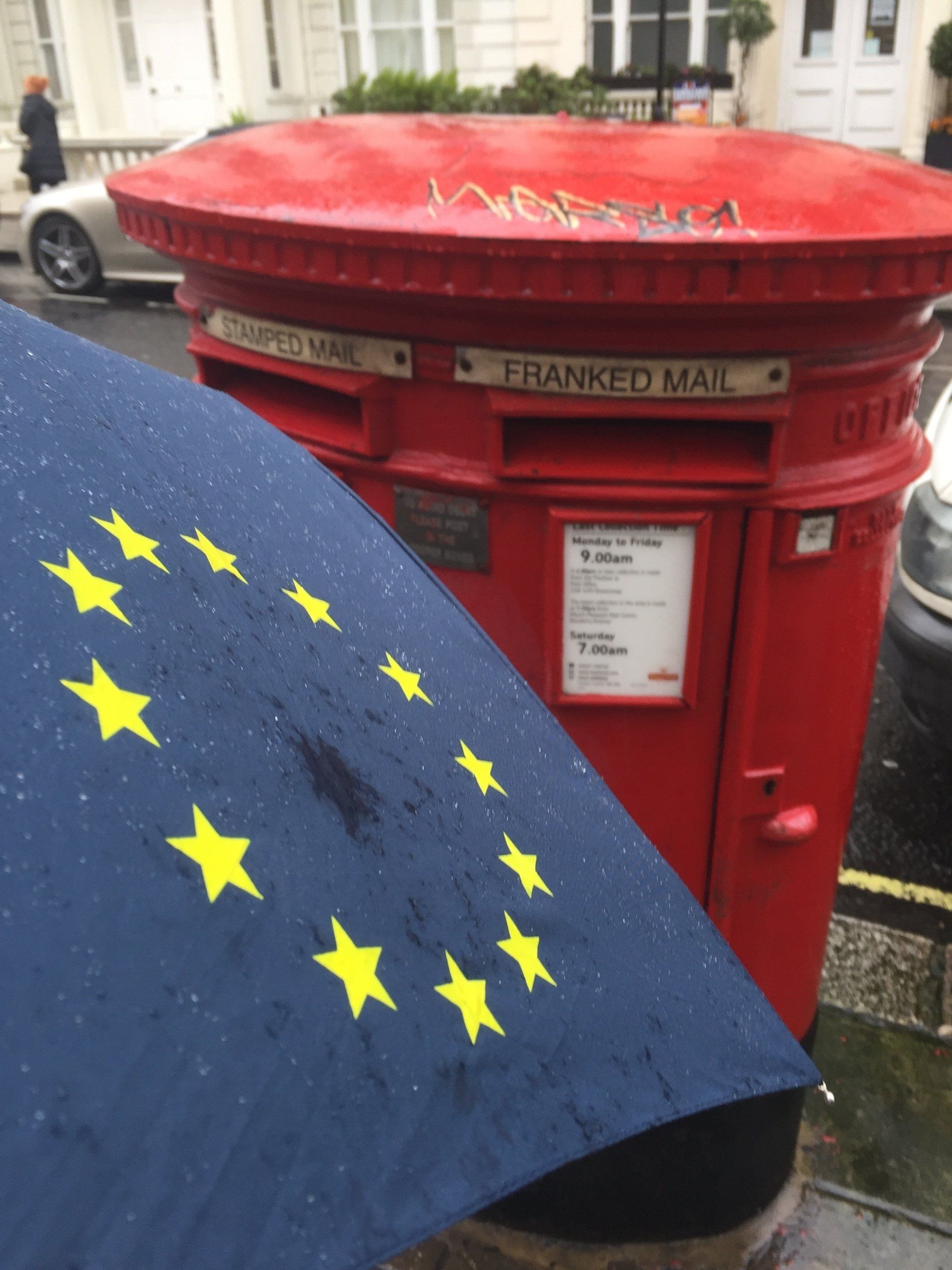 Ein roter Briefkasten mit einem blauen Regenschirm davor