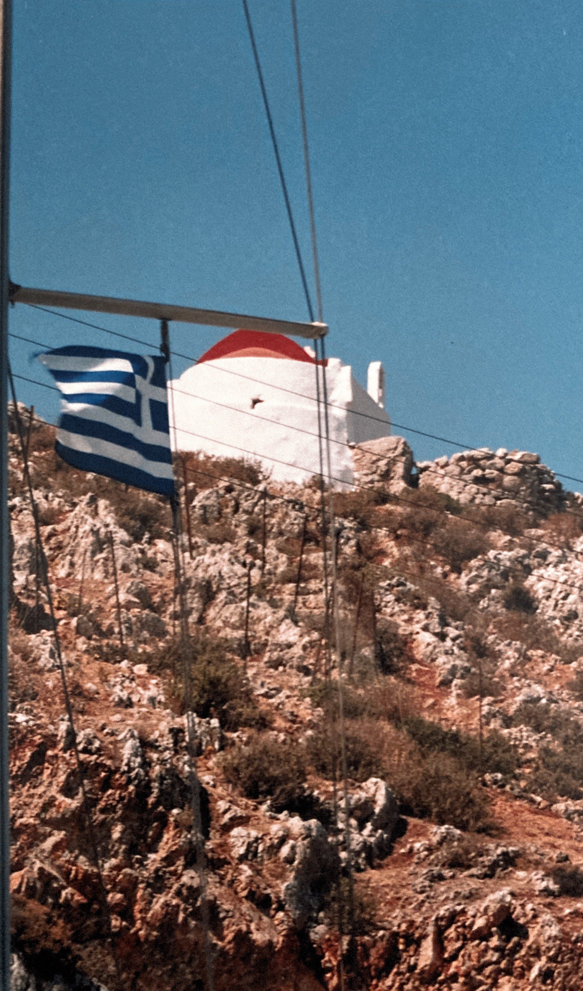 Eine griechische Flagge weht vor einem weißen Gebäude auf einem felsigen Hügel