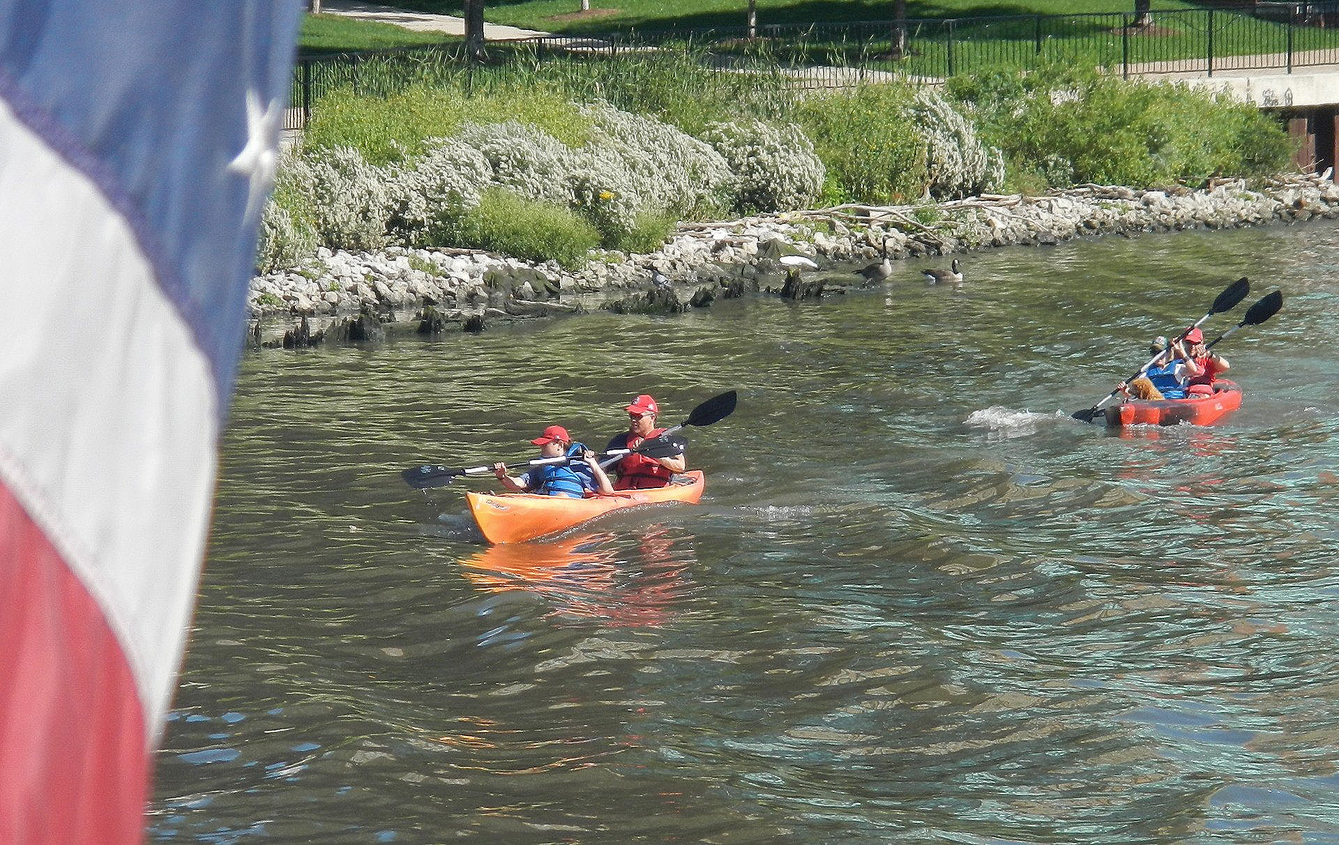 Zwei Personen in Kajaks auf einem Fluss mit einer amerikanischen Flagge im Vordergrund