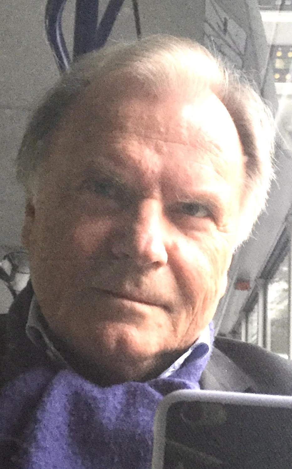 Ein Mann mit einem lila Schal hält ein Mobiltelefon.