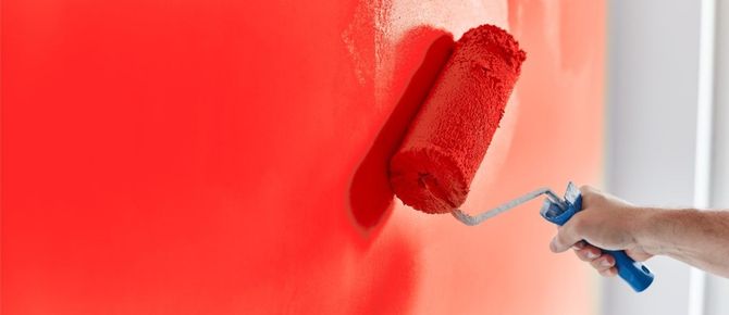 Person painting a red wall with a paint roller