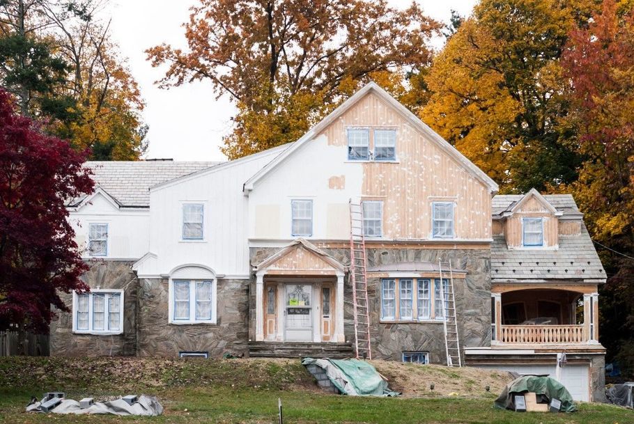 Large old farmhouse with white siding and stone facade, framed by autumn trees and a front porch