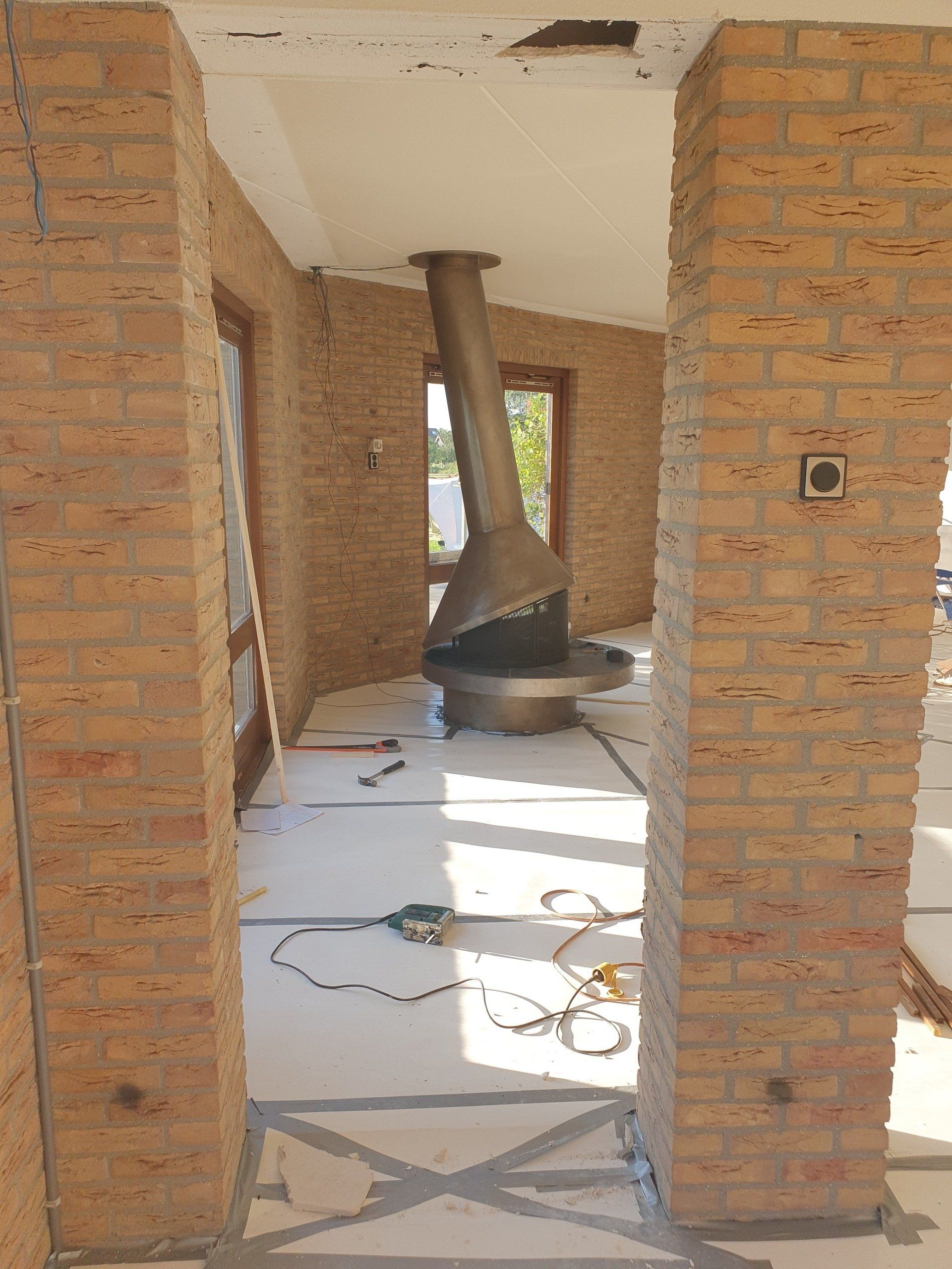 Bakstenen hal met een zwarte metalen open haard die door het plafond ventileert, bouwmaterialen op de vloer