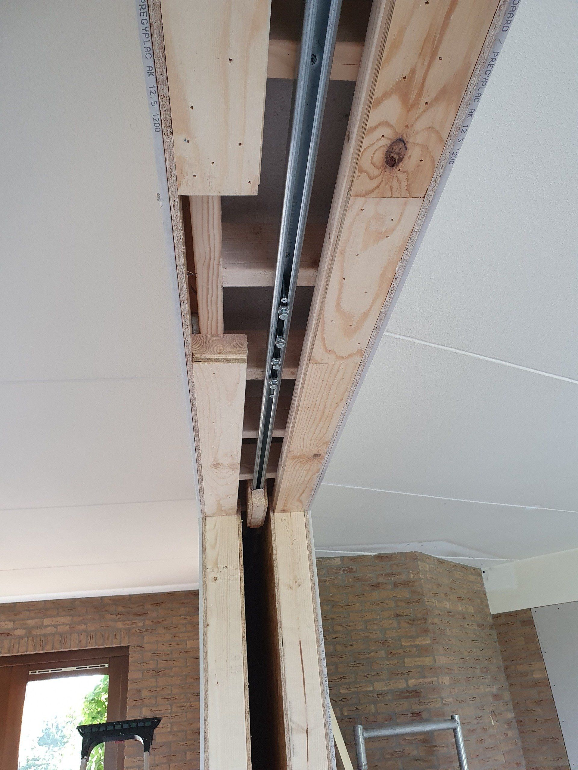 Zichtbare plafondbalk met metalen buis en opening in een onafgewerkte kamer