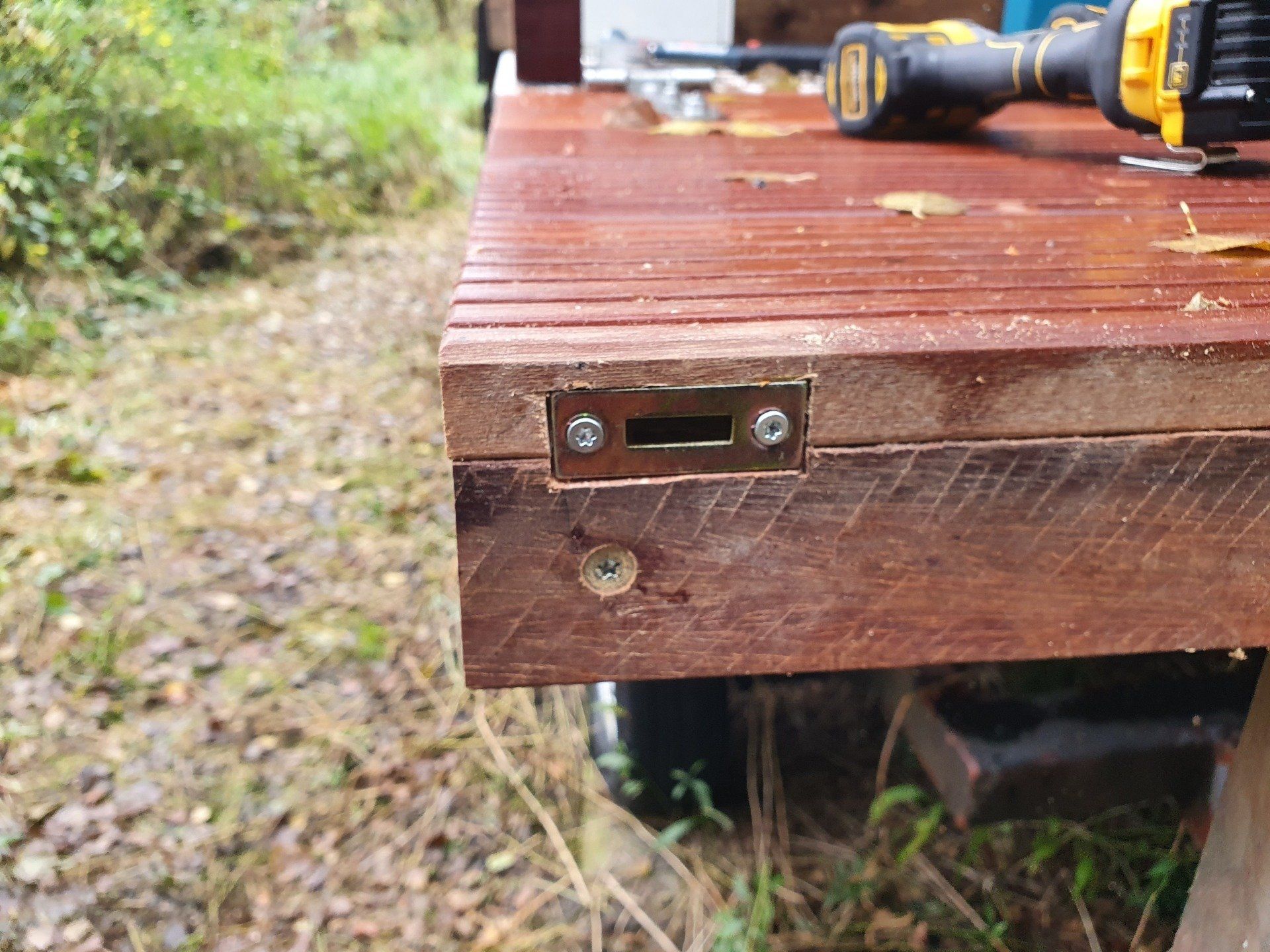 Bruine houten terrashoek met een geel-zwarte boormachine erop, buiten