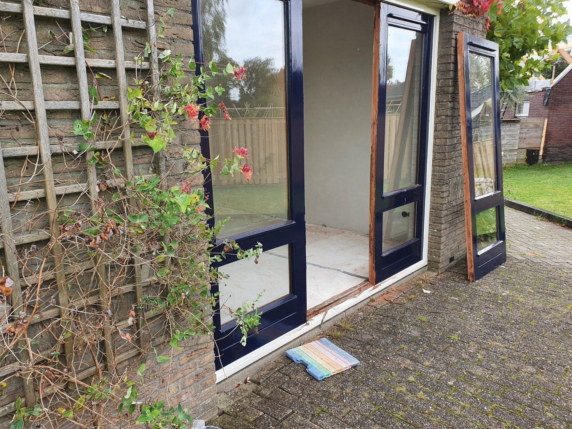 Openslaande glazen terrasdeuren naast een met klimplanten begroeide schutting op een grindterras.