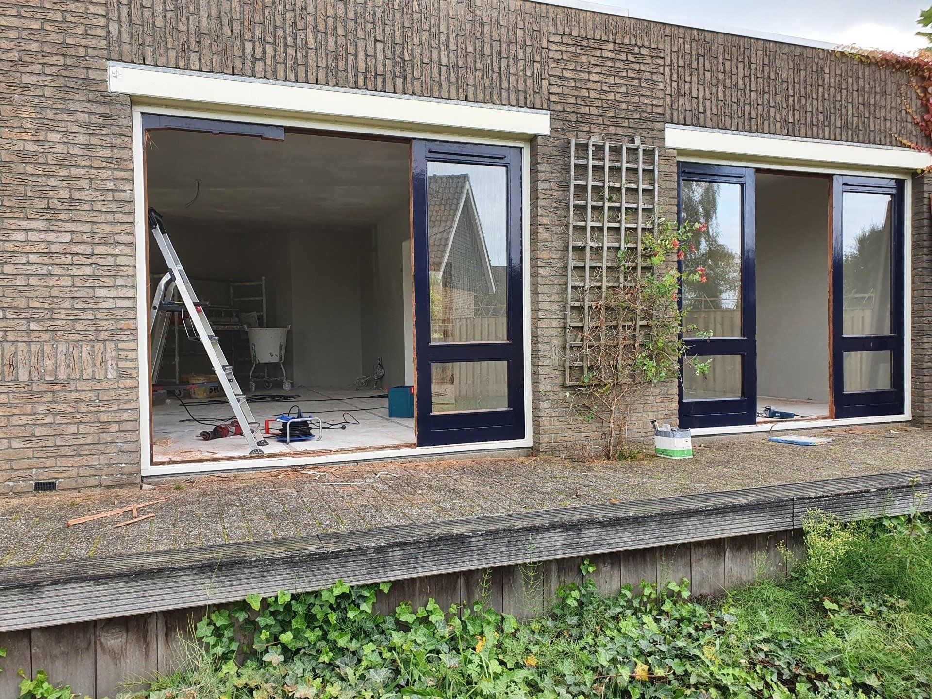 Buitenkant van het gebouw met grote raamopeningen en glazen deuren tijdens de renovatie.
