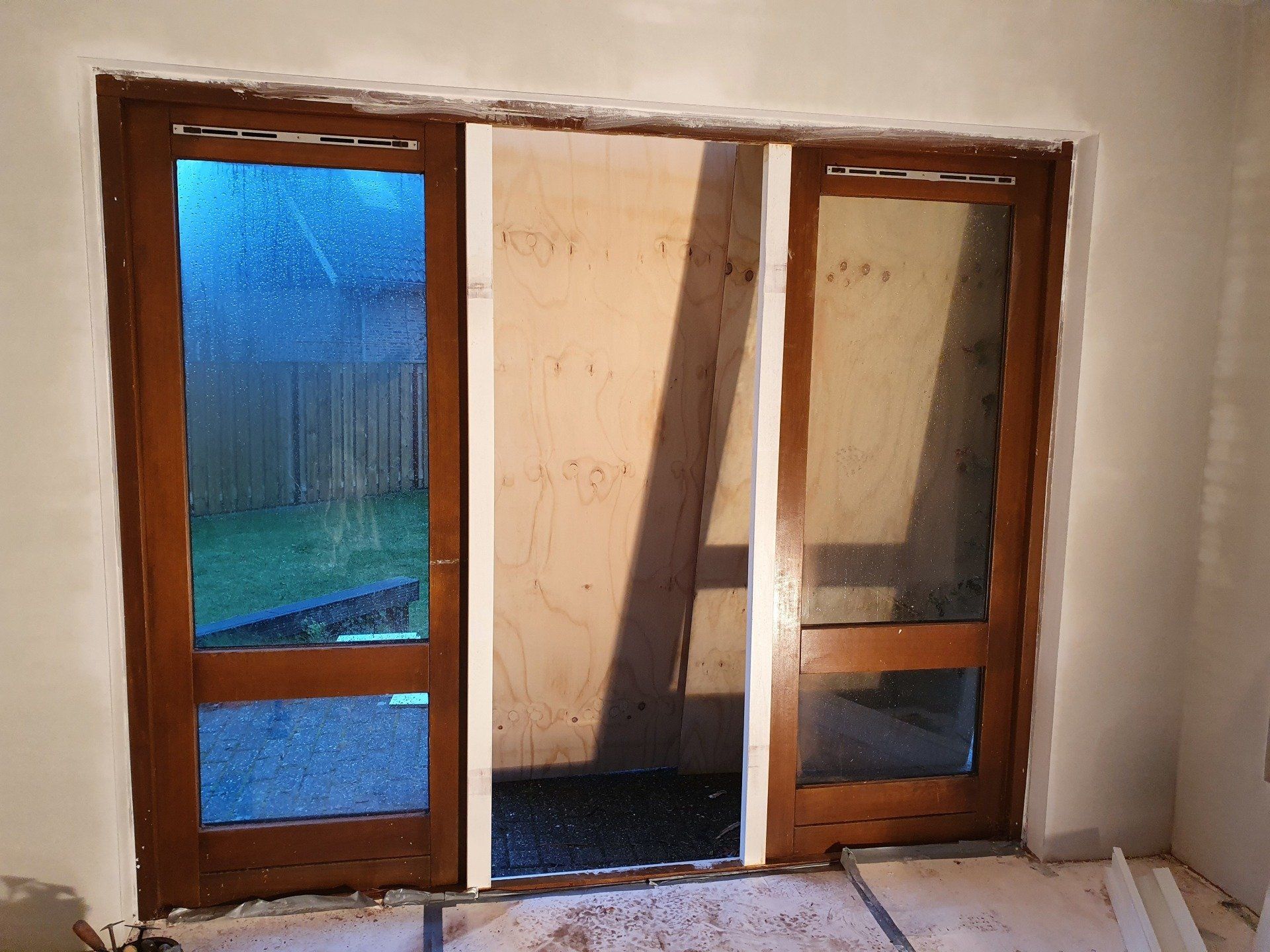 Deels geopende houten schuifdeuren die toegang geven tot een patio, met links een blauw getint glazen paneel.