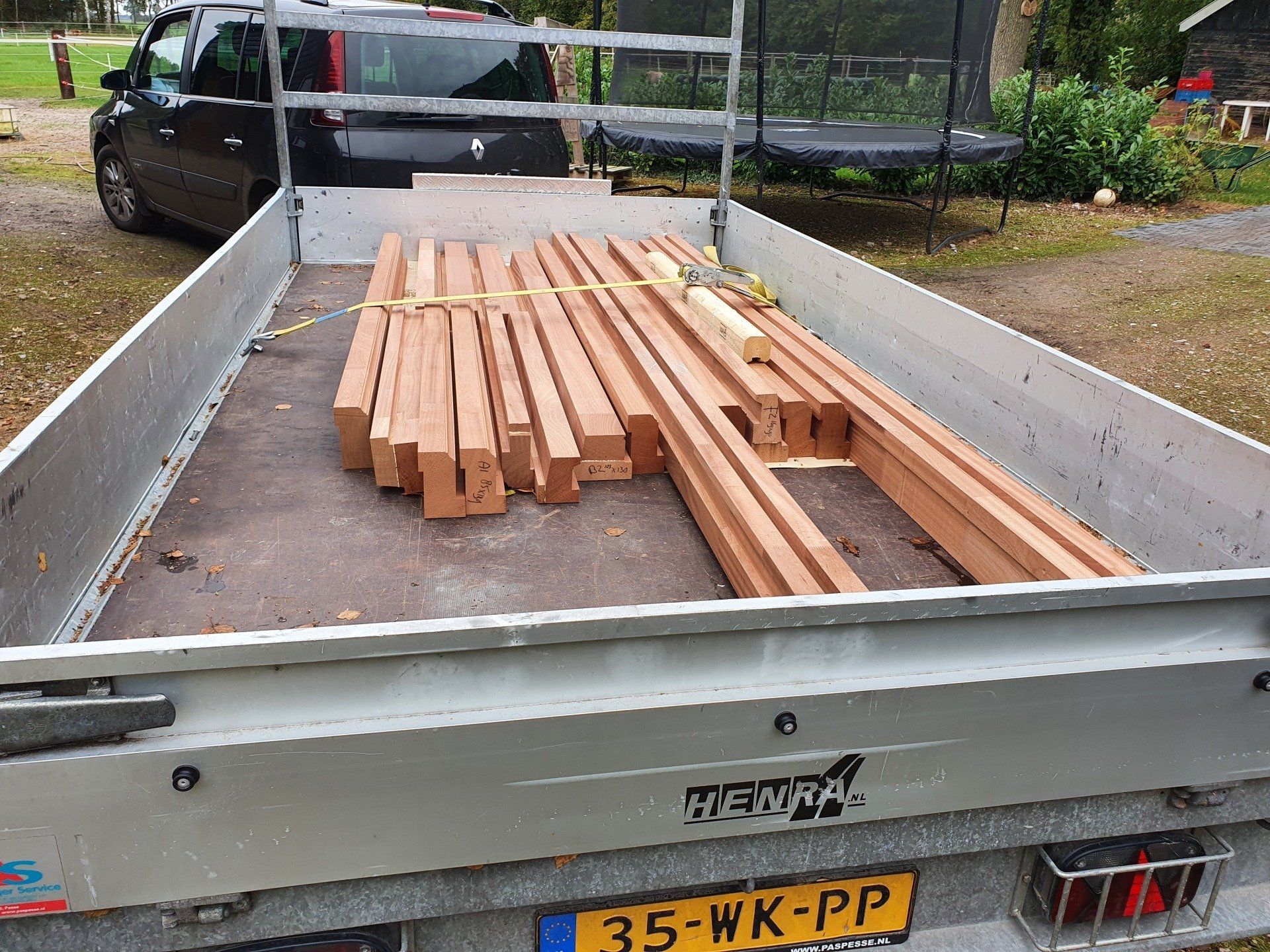 Een vrachtwagen met open laadbak vervoert gestapelde houten balken en planken op een bouwterrein.