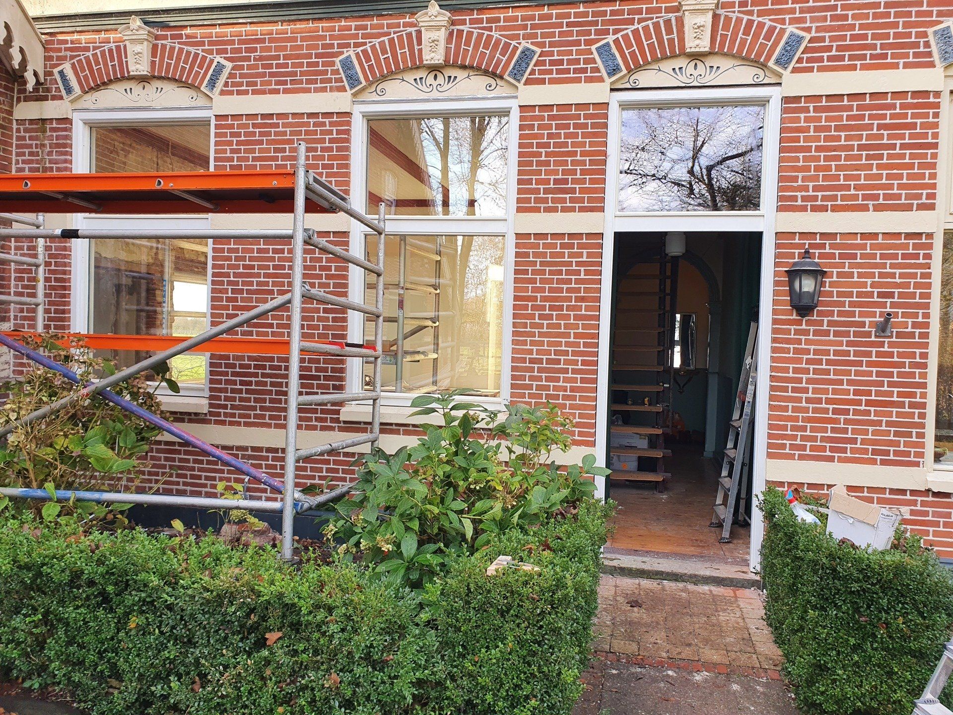 Ingang van een bakstenen herenhuis met open deur, raam en steigers voor het gebouw.