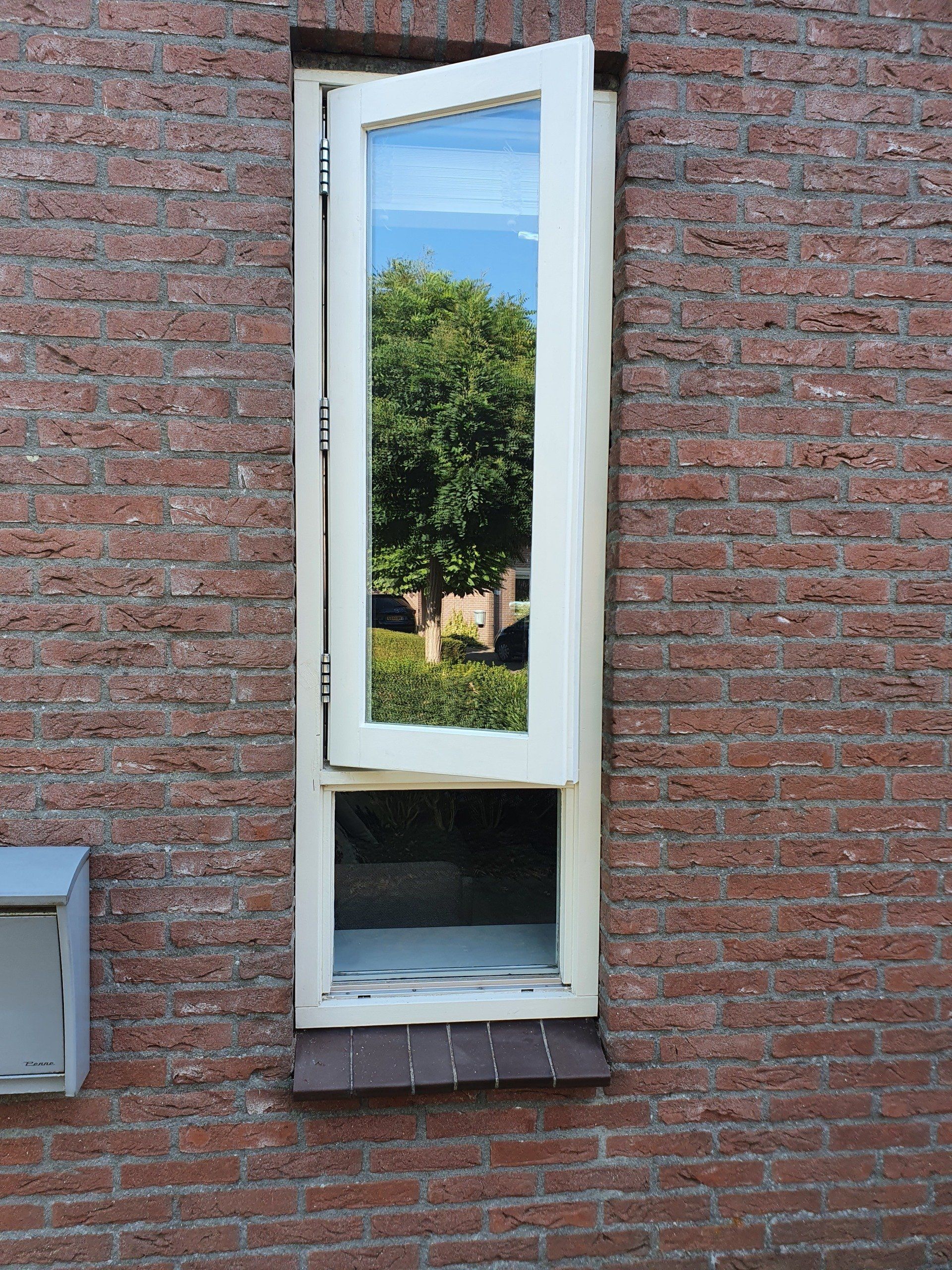 Een open raam in een bakstenen muur biedt uitzicht op een boom en de blauwe lucht.