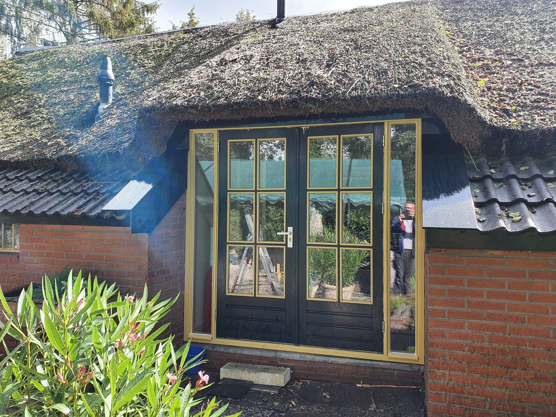 Ingang van een huisje met rieten dak, houten kozijnen met glazen deuren en rode bakstenen muren.