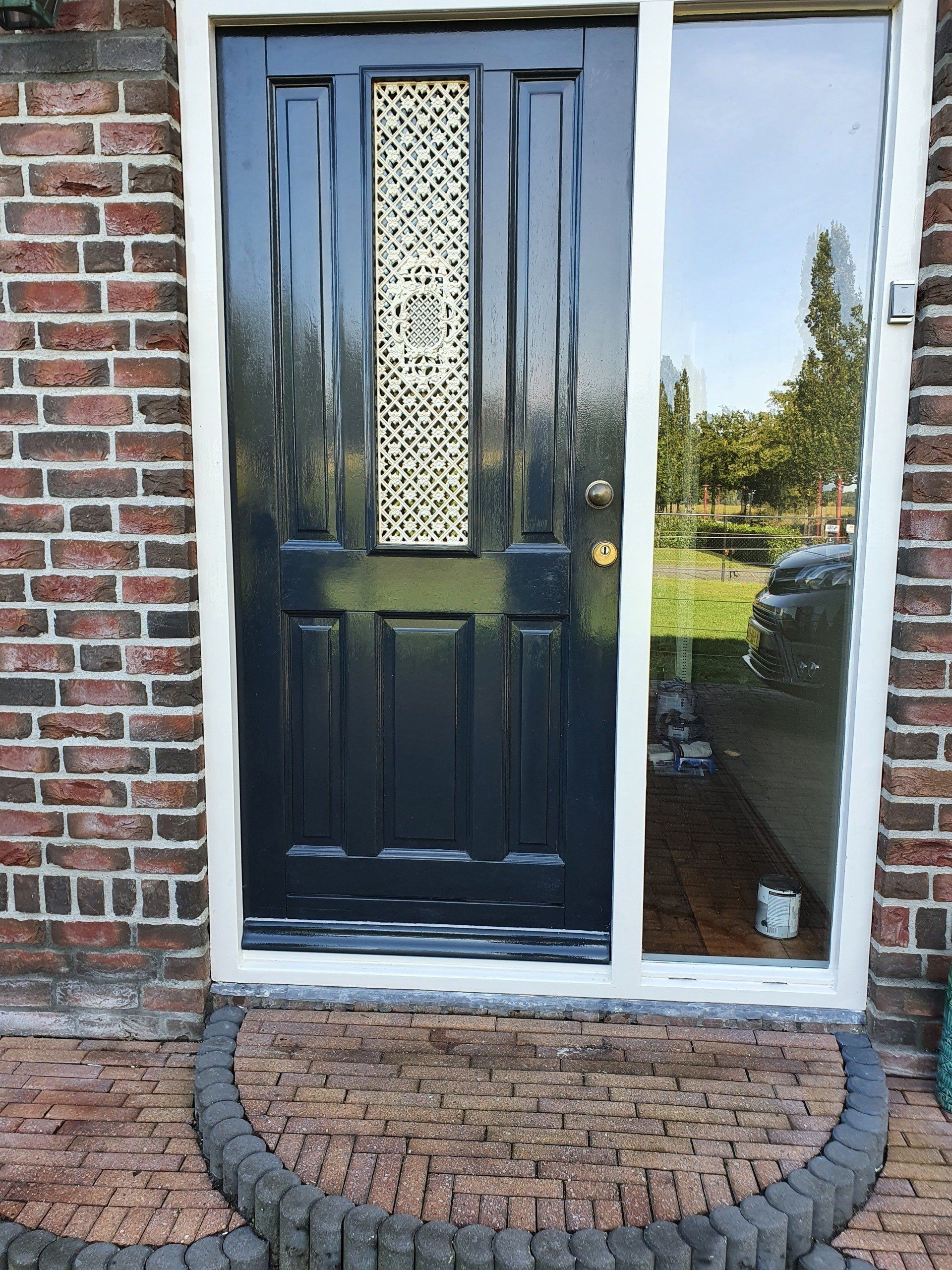 Zwarte voordeur met decoratief glaspaneel en bakstenen stoep naast een bakstenen muur.