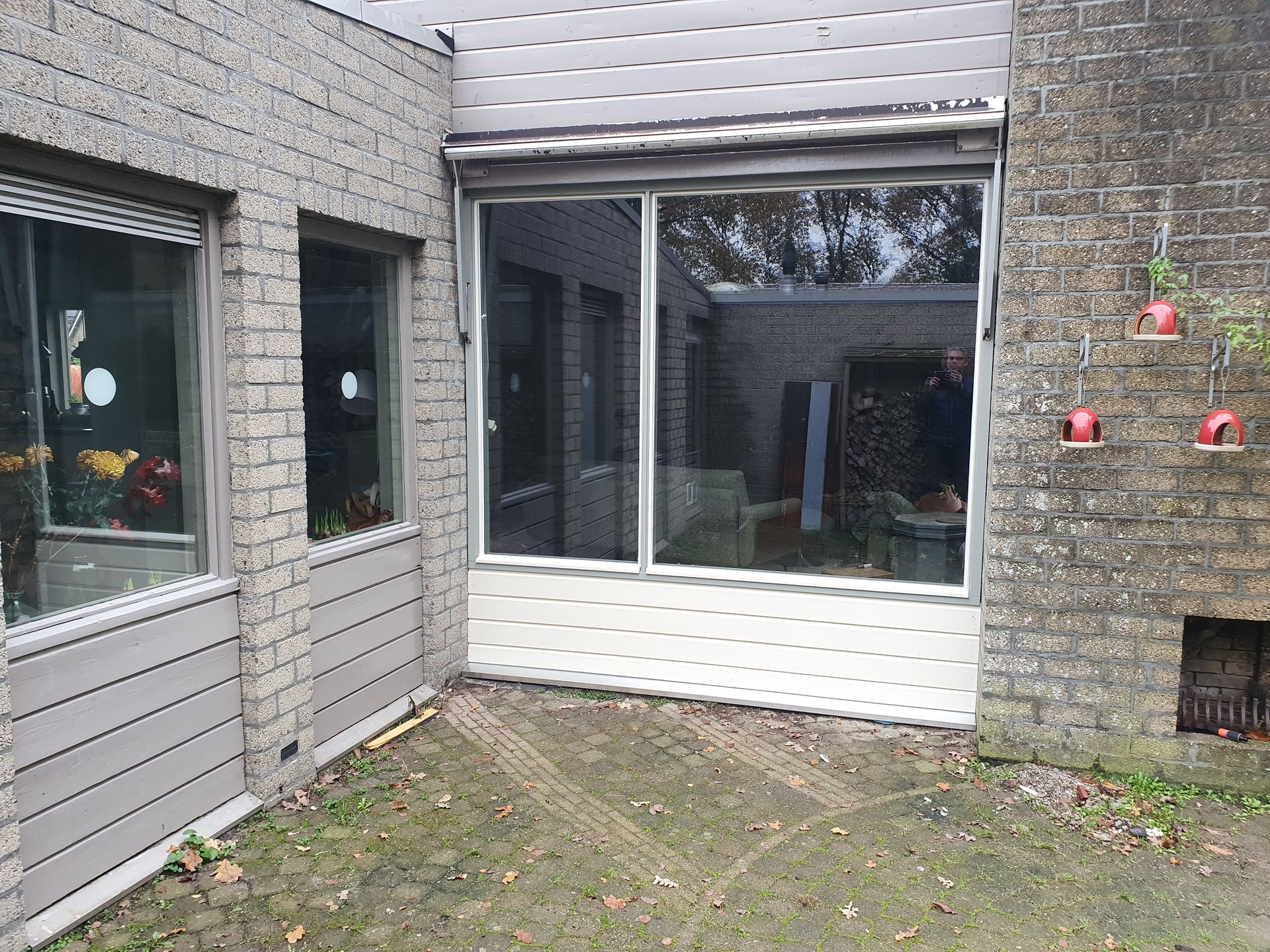 Binnenplaats met patio tussen bakstenen muren, grote ramen, een glazen schuifdeur en kleine decoratieve lampjes.