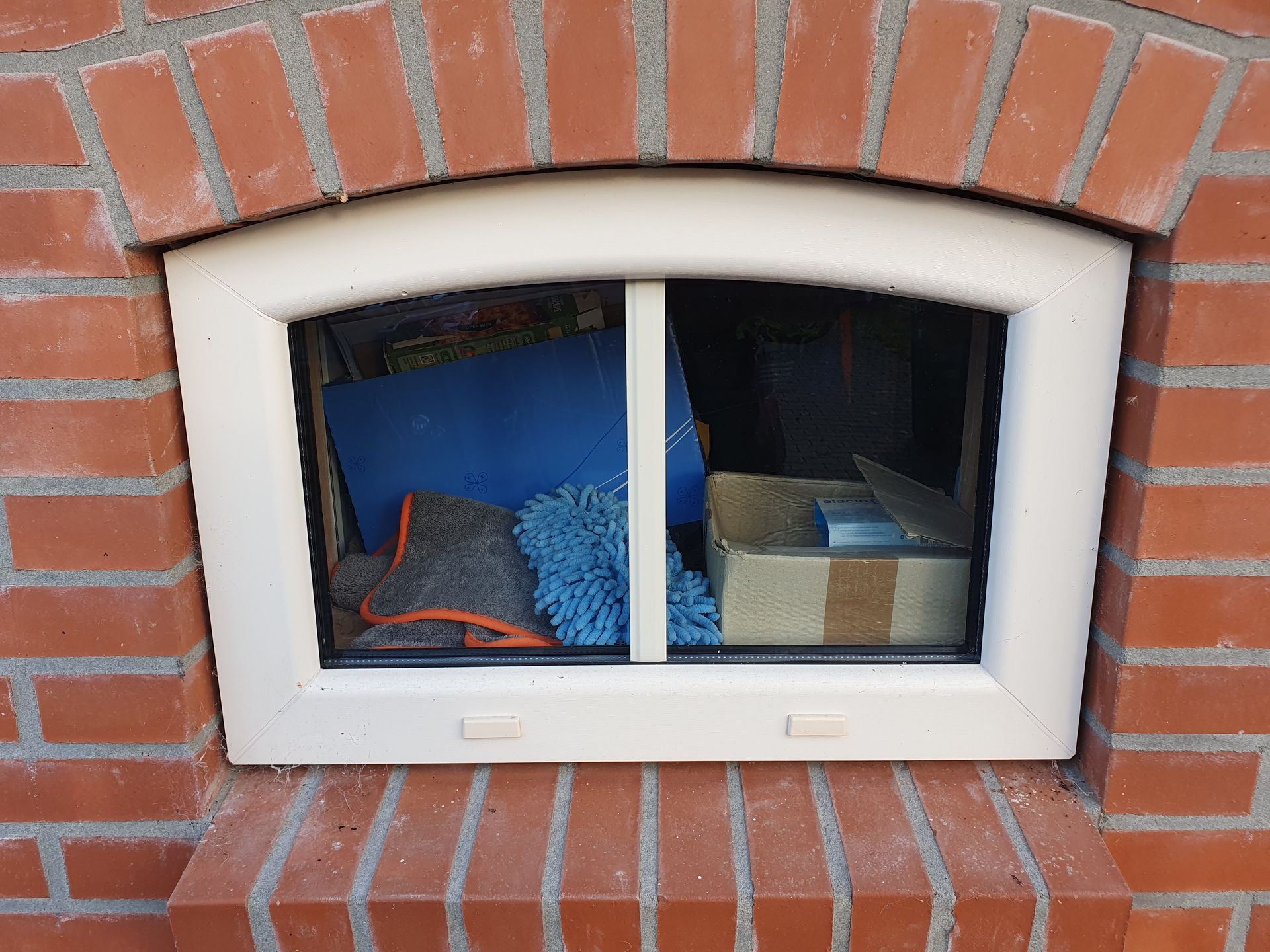 Klein kelderraam in een bakstenen muur, met uitzicht op een blauw betegeld interieur waarin een draadloze telefoon ligt.