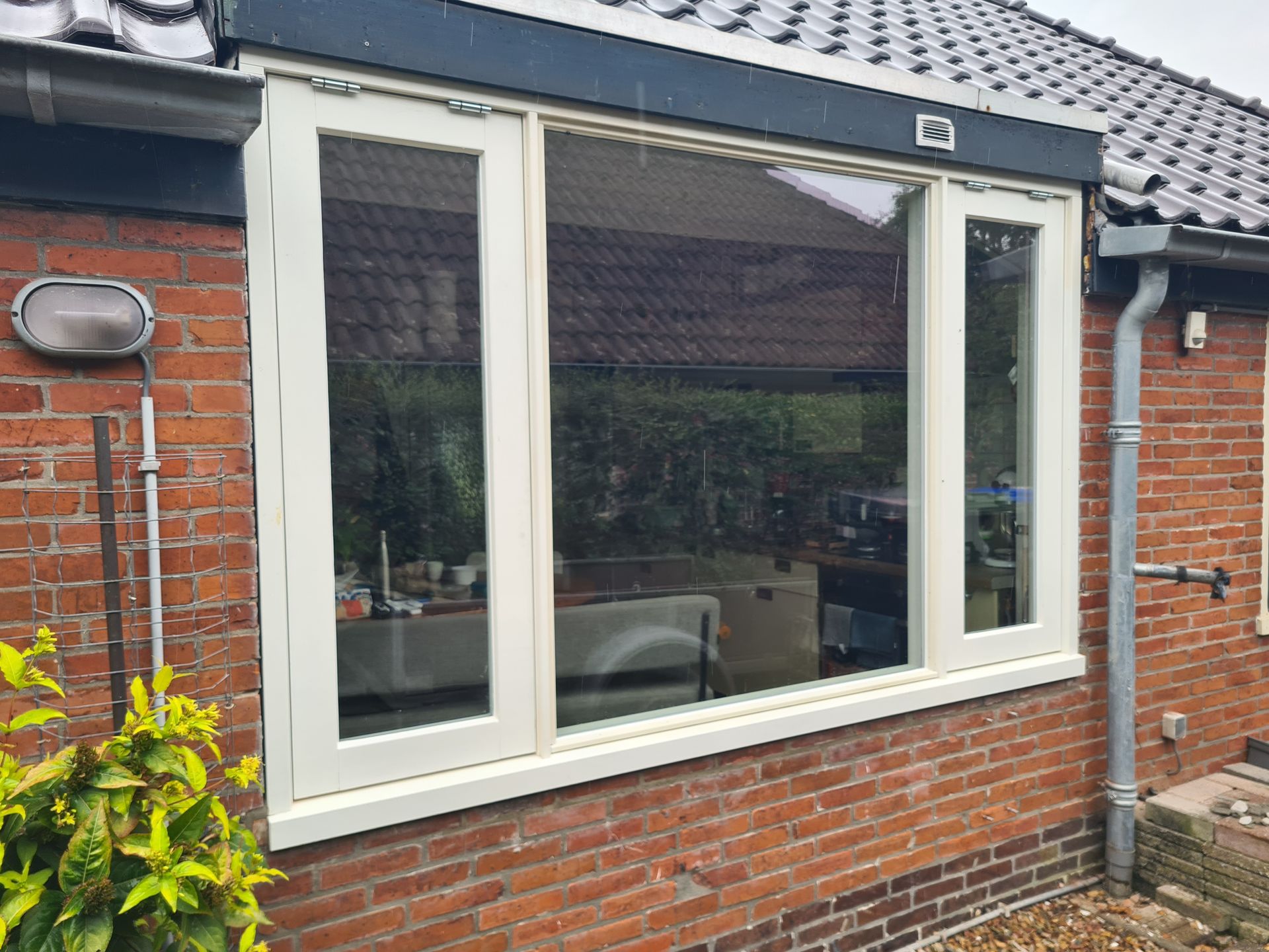 Erker met witte kozijnen in een rood bakstenen huis met een donker dak en een tuin eronder.
