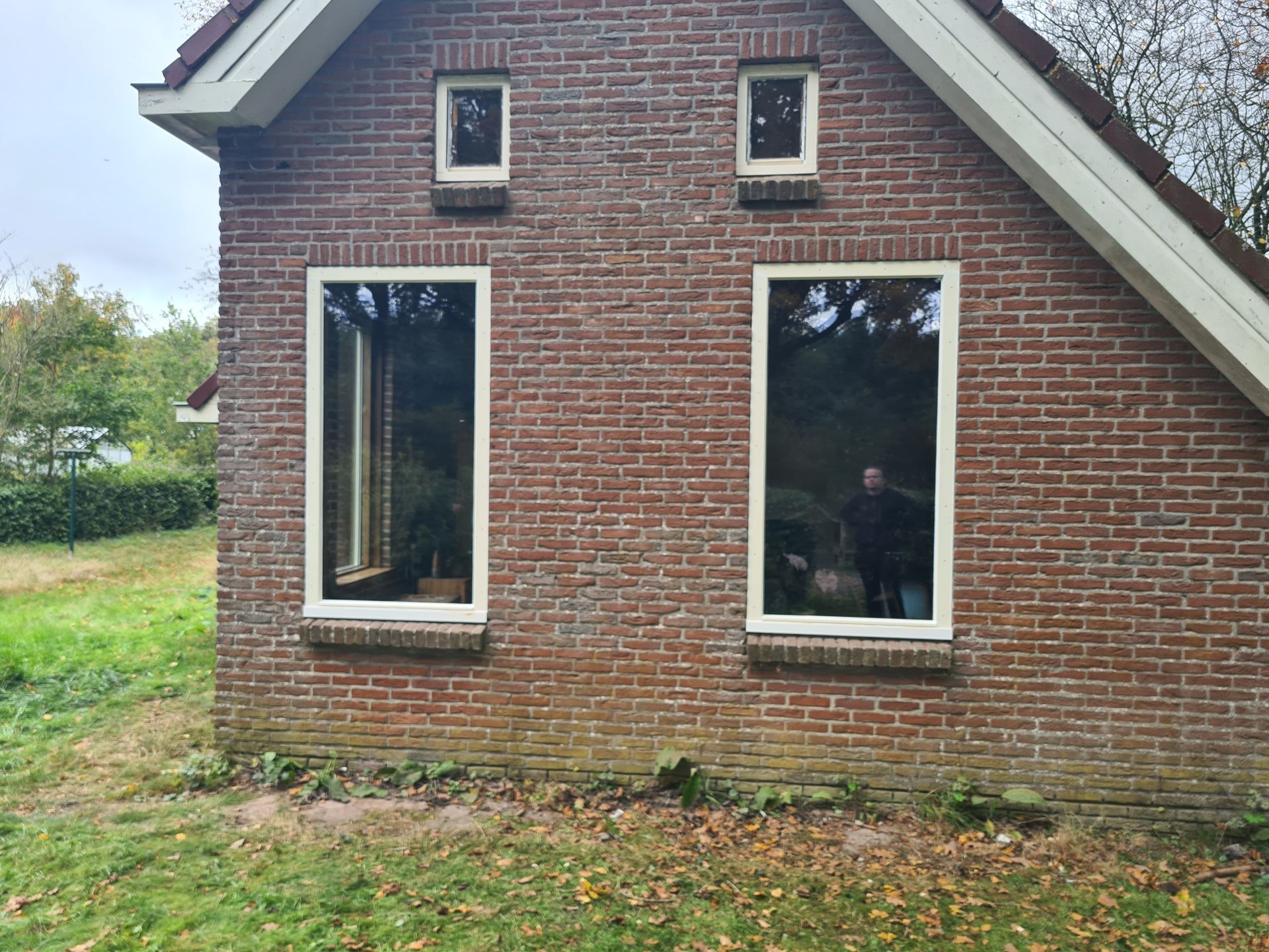 De buitenkant van een bakstenen huis met drie ramen en een schuin dak, gezien vanaf de zijkant.
