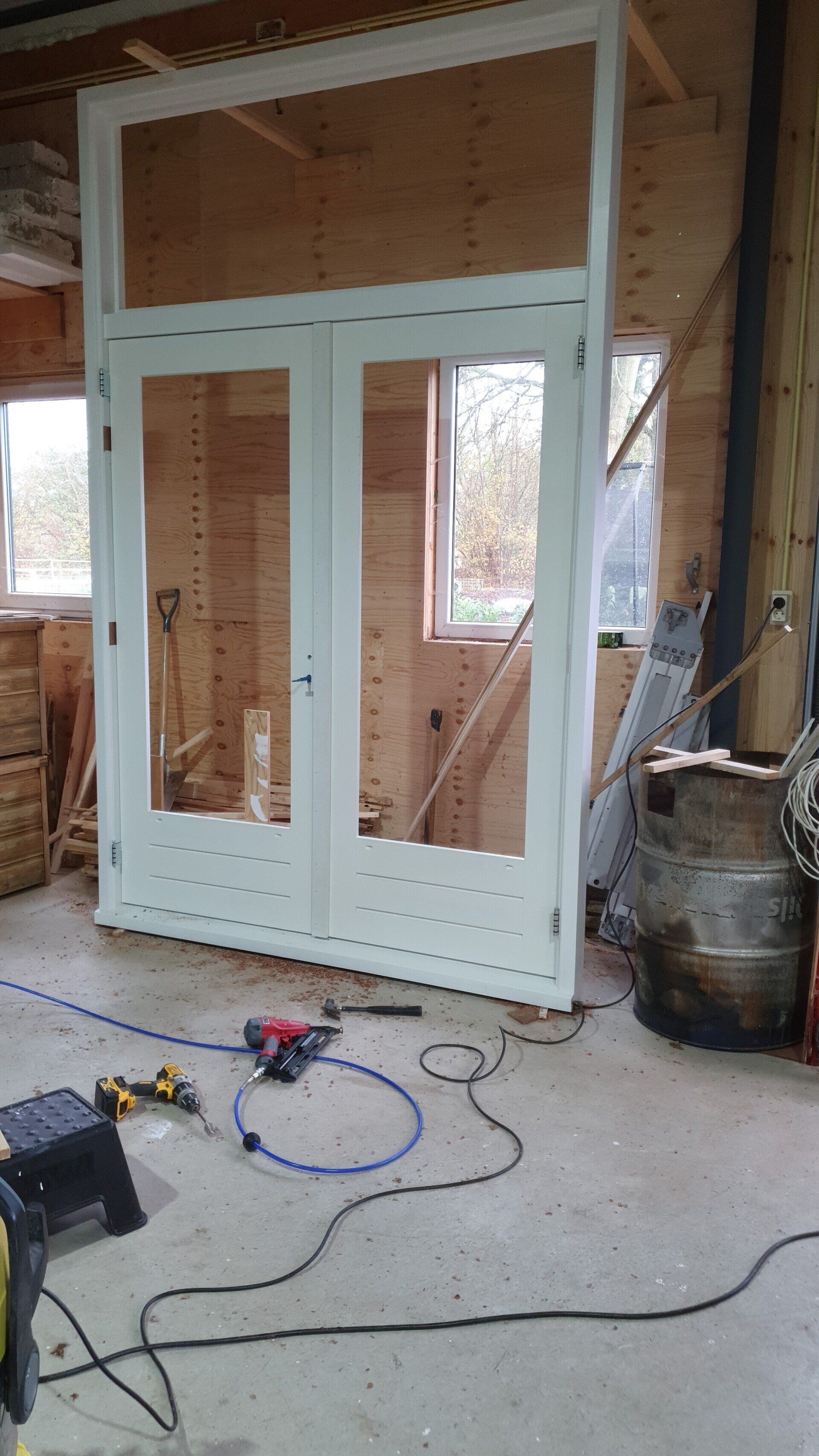 Witte openslaande deuren geplaatst in een nog in aanbouw zijnde constructie, met gereedschap en bedrading op de vloer.