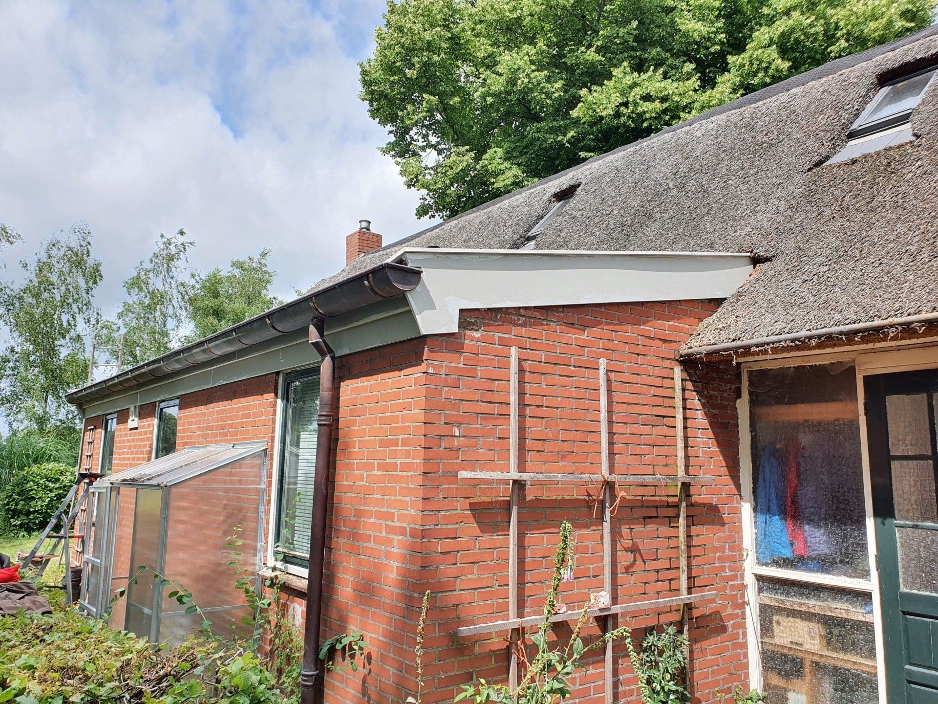 Een rood bakstenen huis met een rieten dak en steigers langs de zijkant, onder een gedeeltelijk bewolkte hemel.