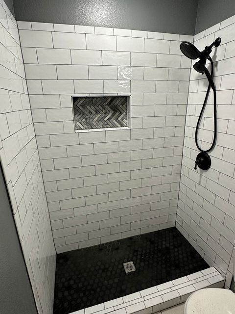 White tiled shower with dark floor and black showerhead, featuring an inset shelf with textured tiles.