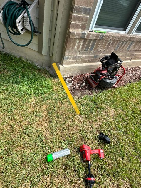 Green grass, a yellow level, and red tools near a building corner.