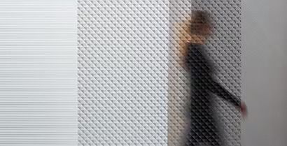 Blurred person in dark clothing walking past a white patterned wall
