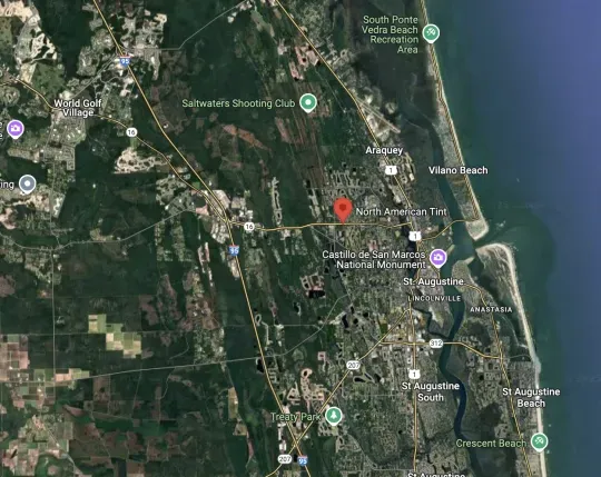 Satellite map of a coastal town with a red location pin near the shoreline and roads inland