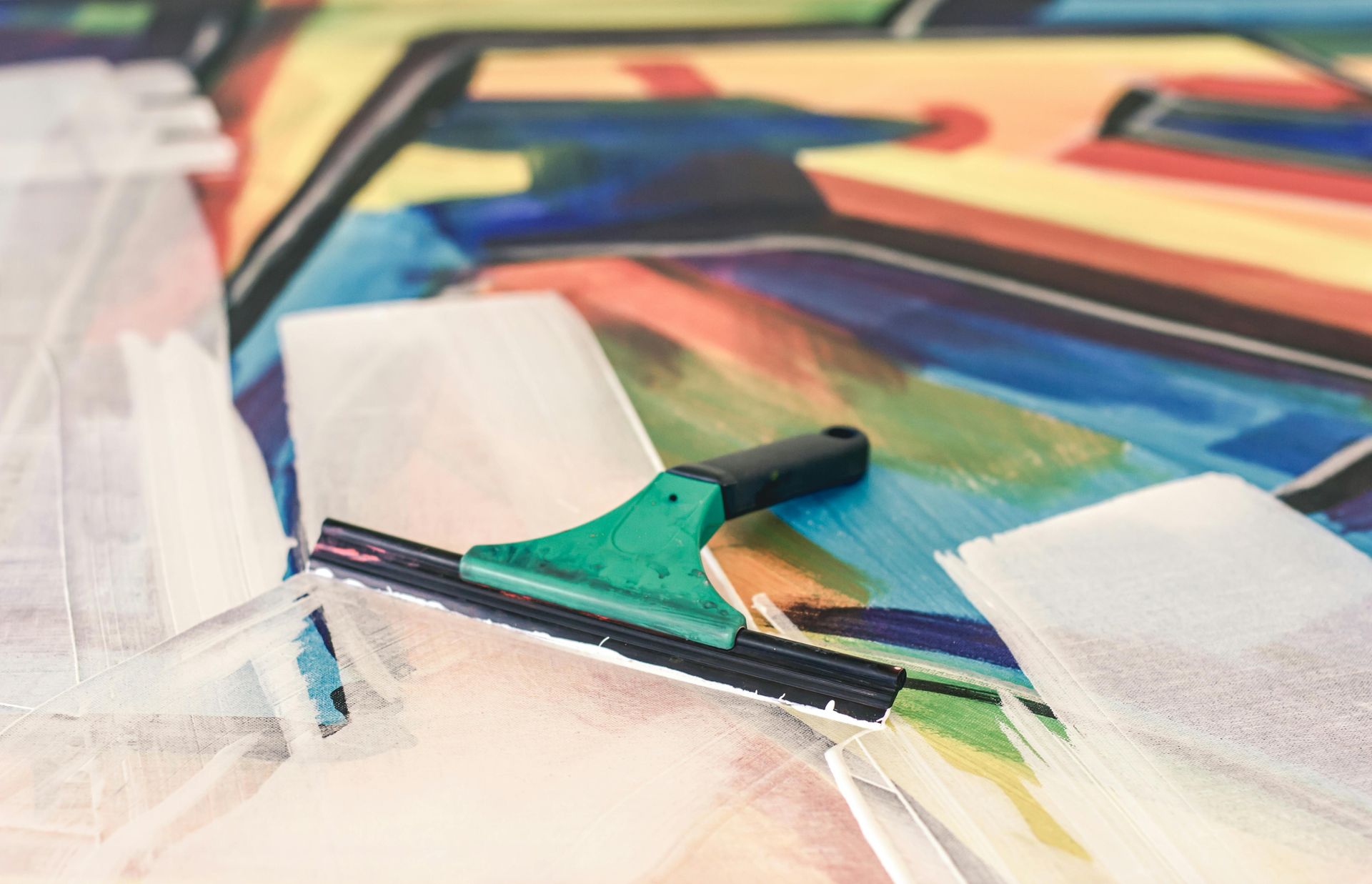 Paintbrush with green handle resting on colorful abstract painted paper and white tape strips