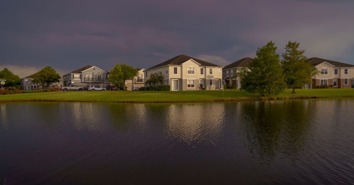 Suburban homes across a calm pond at dusk, with trees and clouds reflected in the water