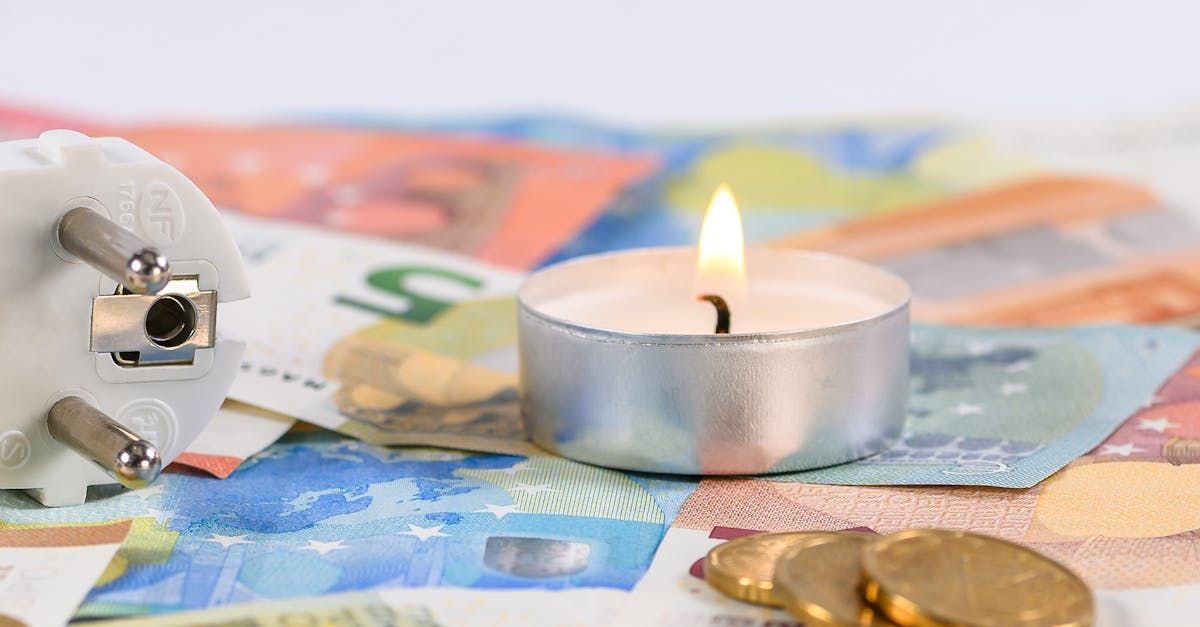 Lit tealight on scattered euro banknotes and coins with a broken plug adapter nearby