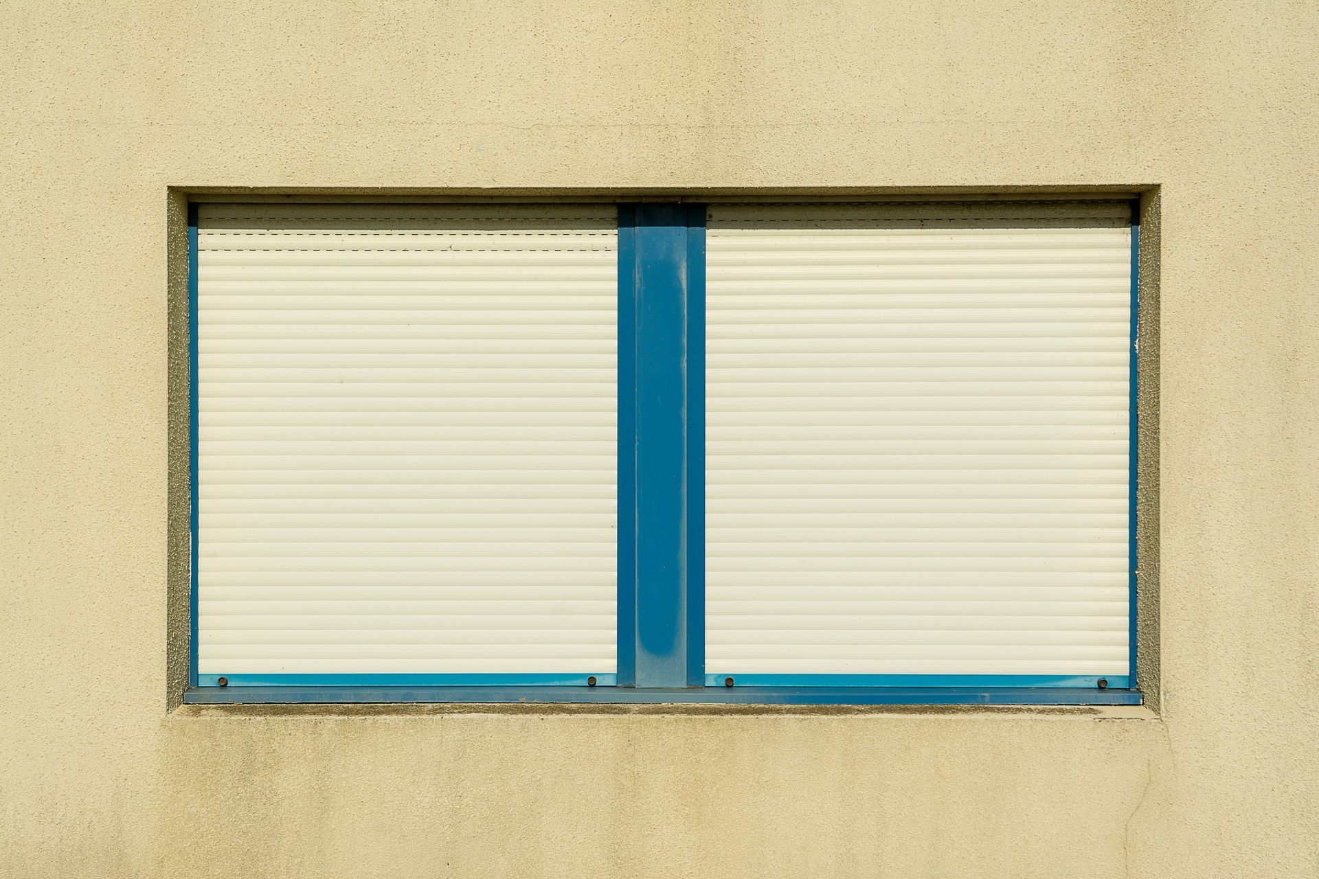Blue-framed window with closed white blinds on a beige wall