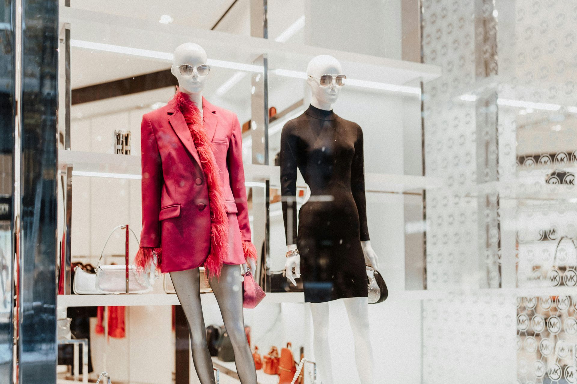 Two mannequins in a boutique display, one in a red blazer and one in a black dress.