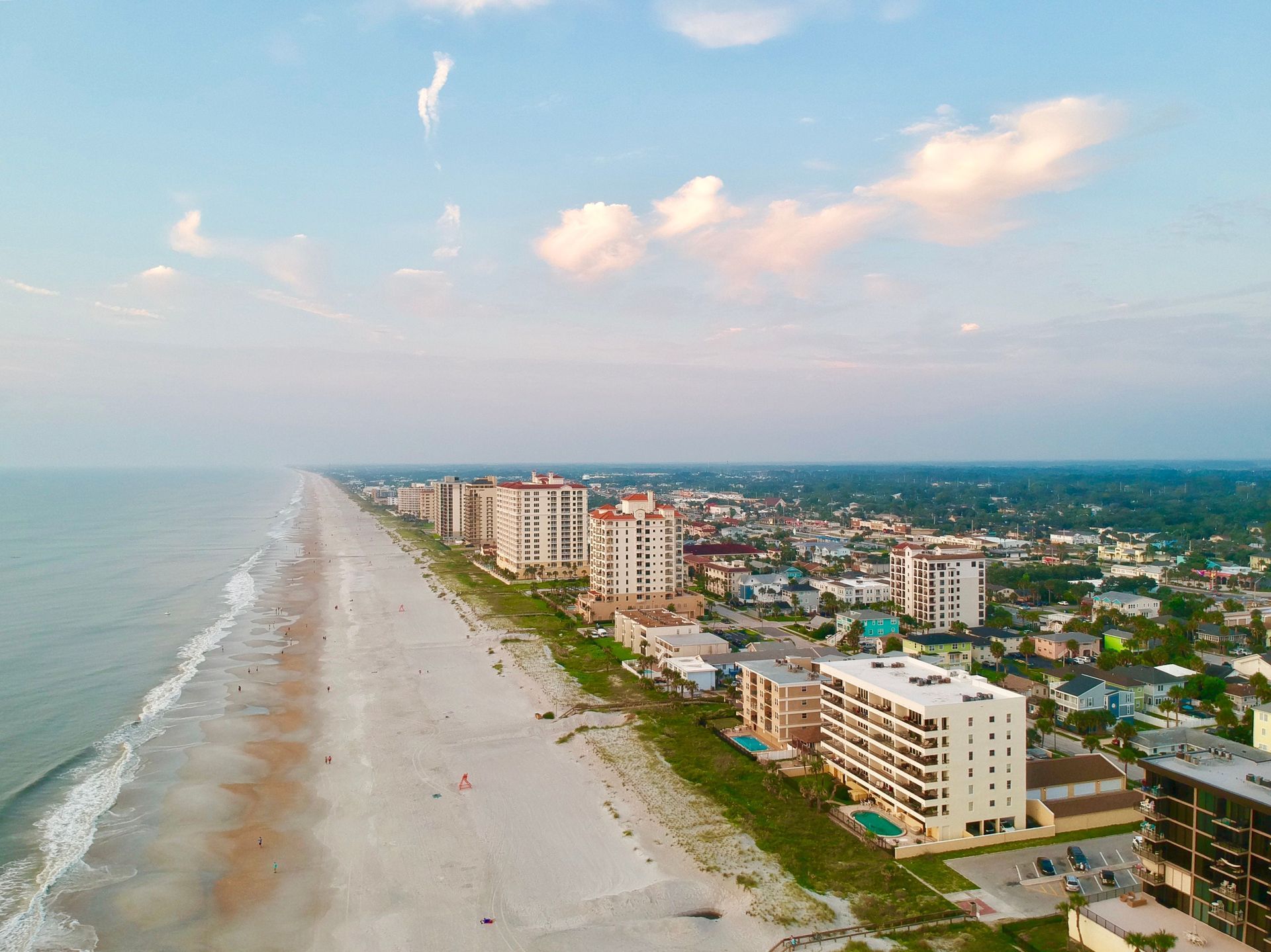 Aerial view of a sandy beach beside a coastal city with apartment buildings and calm blue water