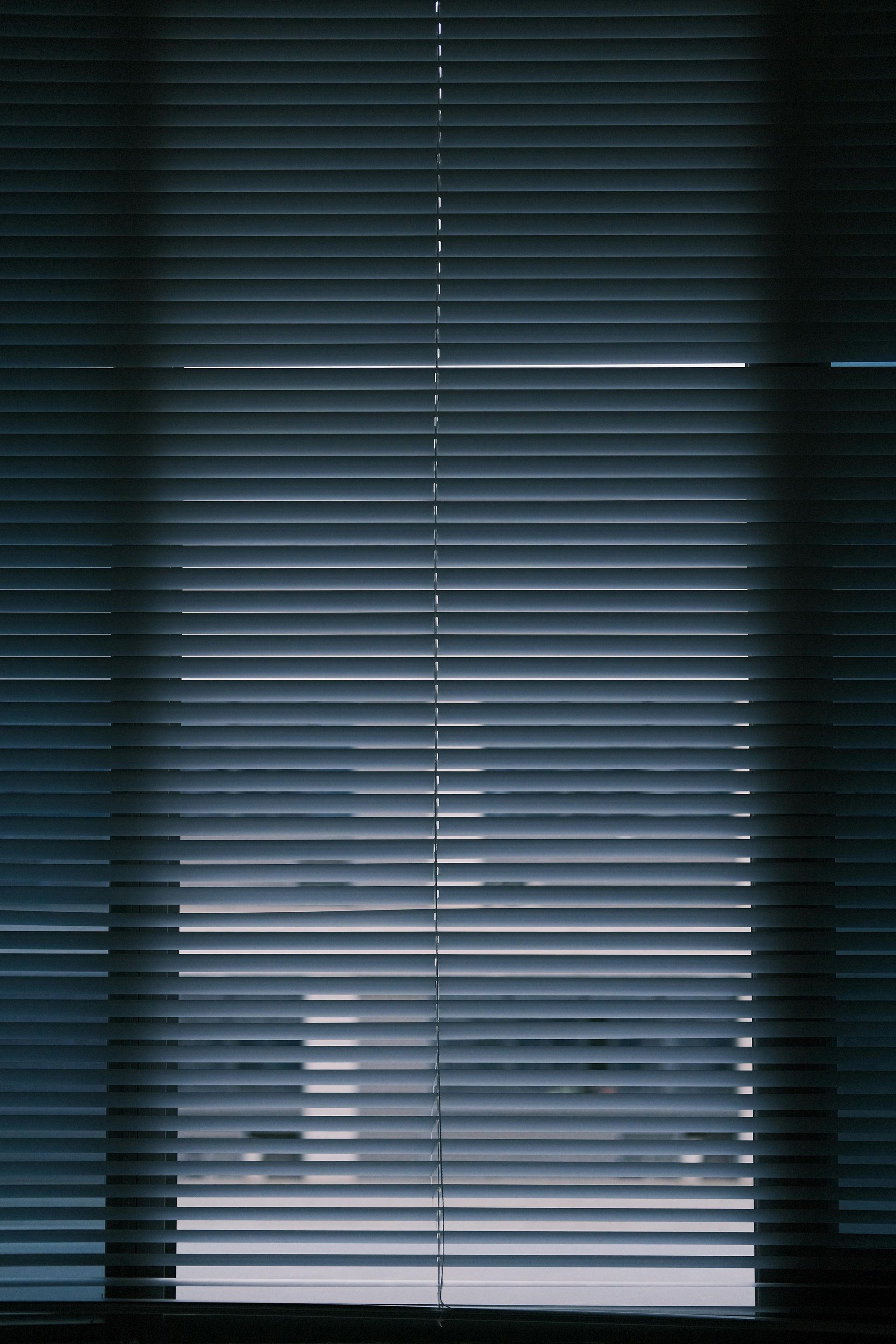 Closed blue window blinds with sunlight filtering through a bright gap at the bottom