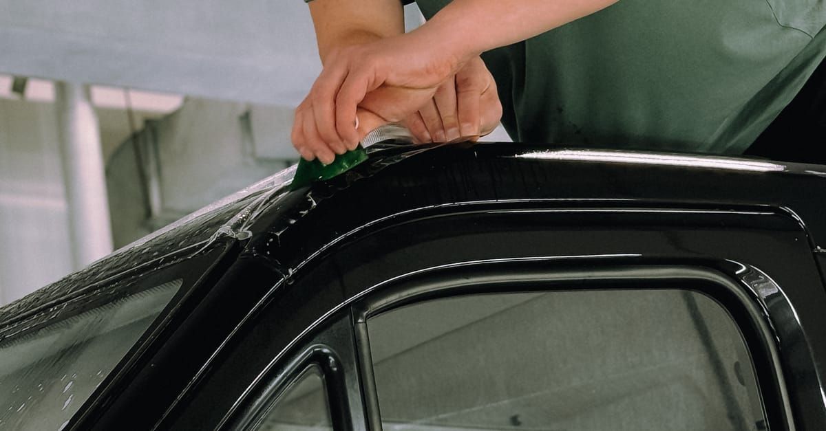 Hand washing the roof of a black car with soap foam in a garage
